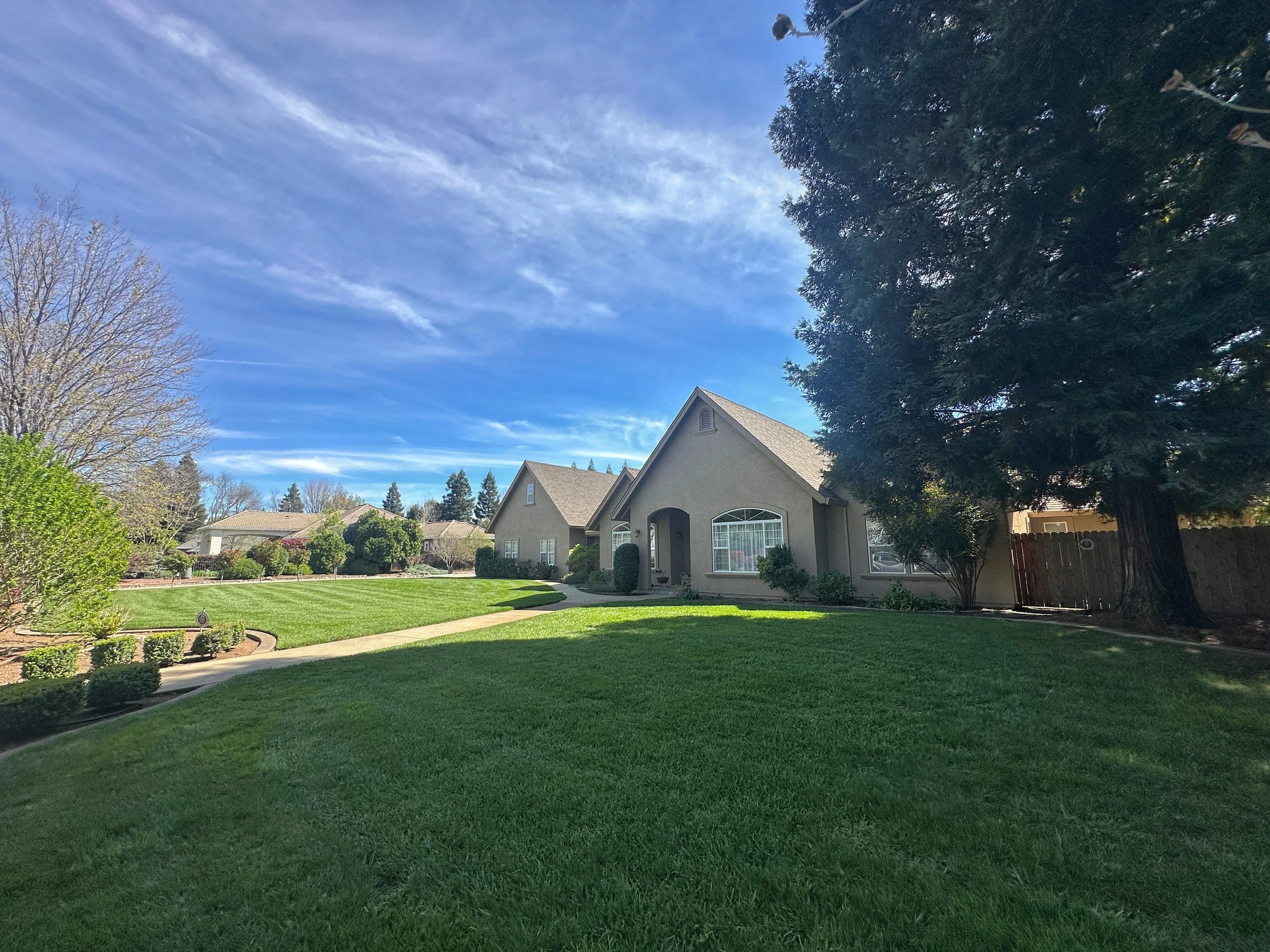 A suburban house with a front yard, green lawn, trees, and a partly cloudy sky.