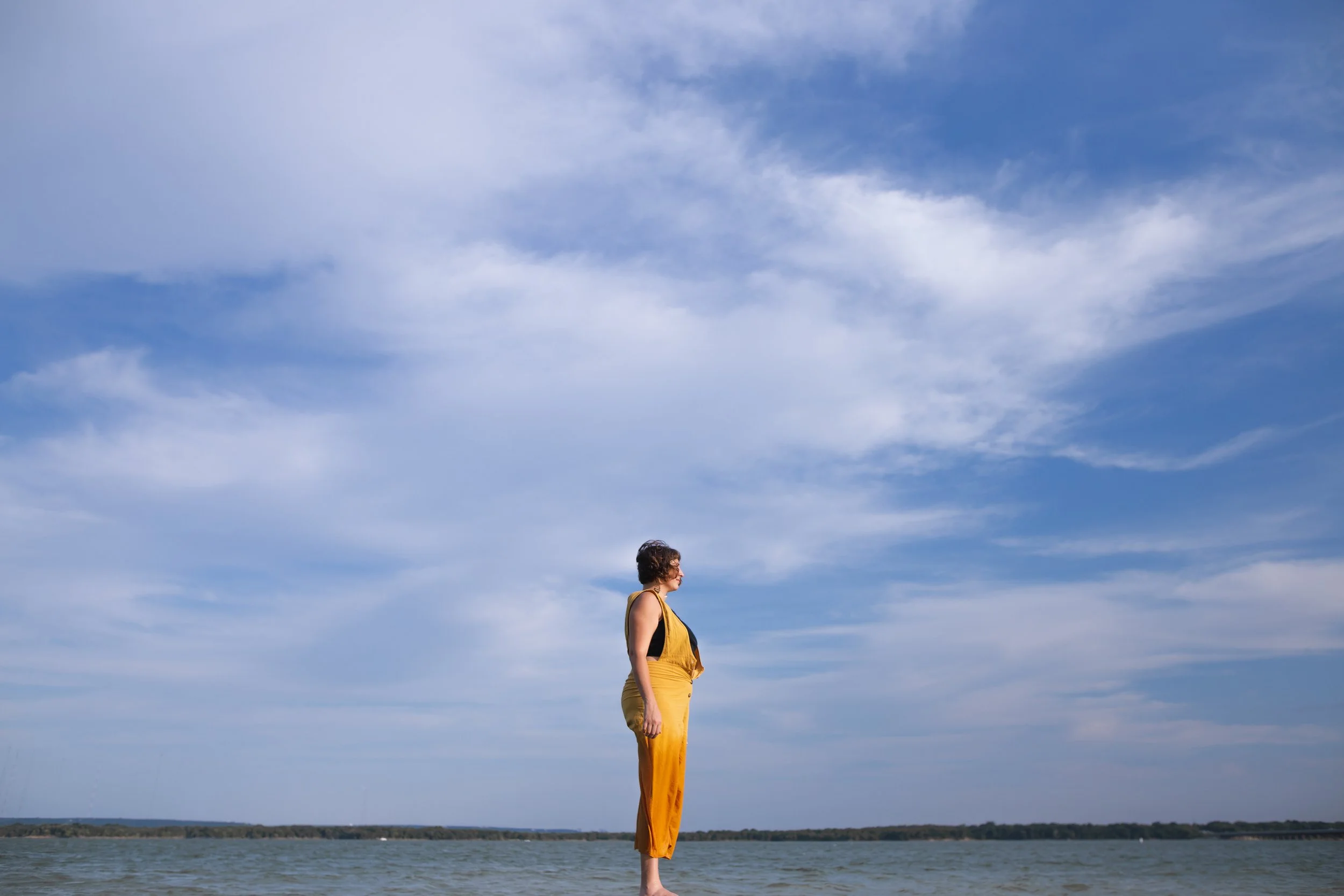 girl in yellow looks at the water with a large blue sky