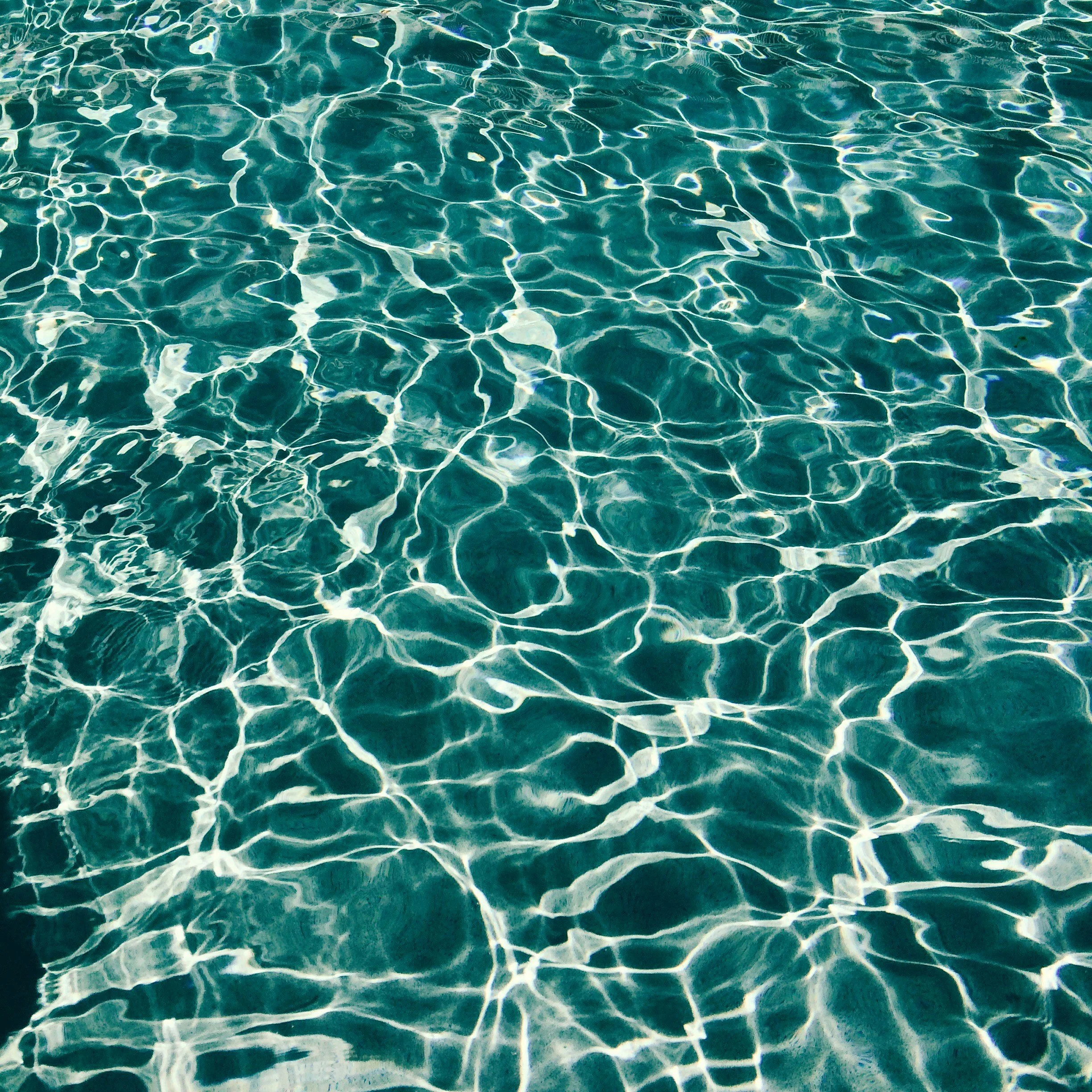Clear swimming pool water with sunlight reflections creating a web of patterns.