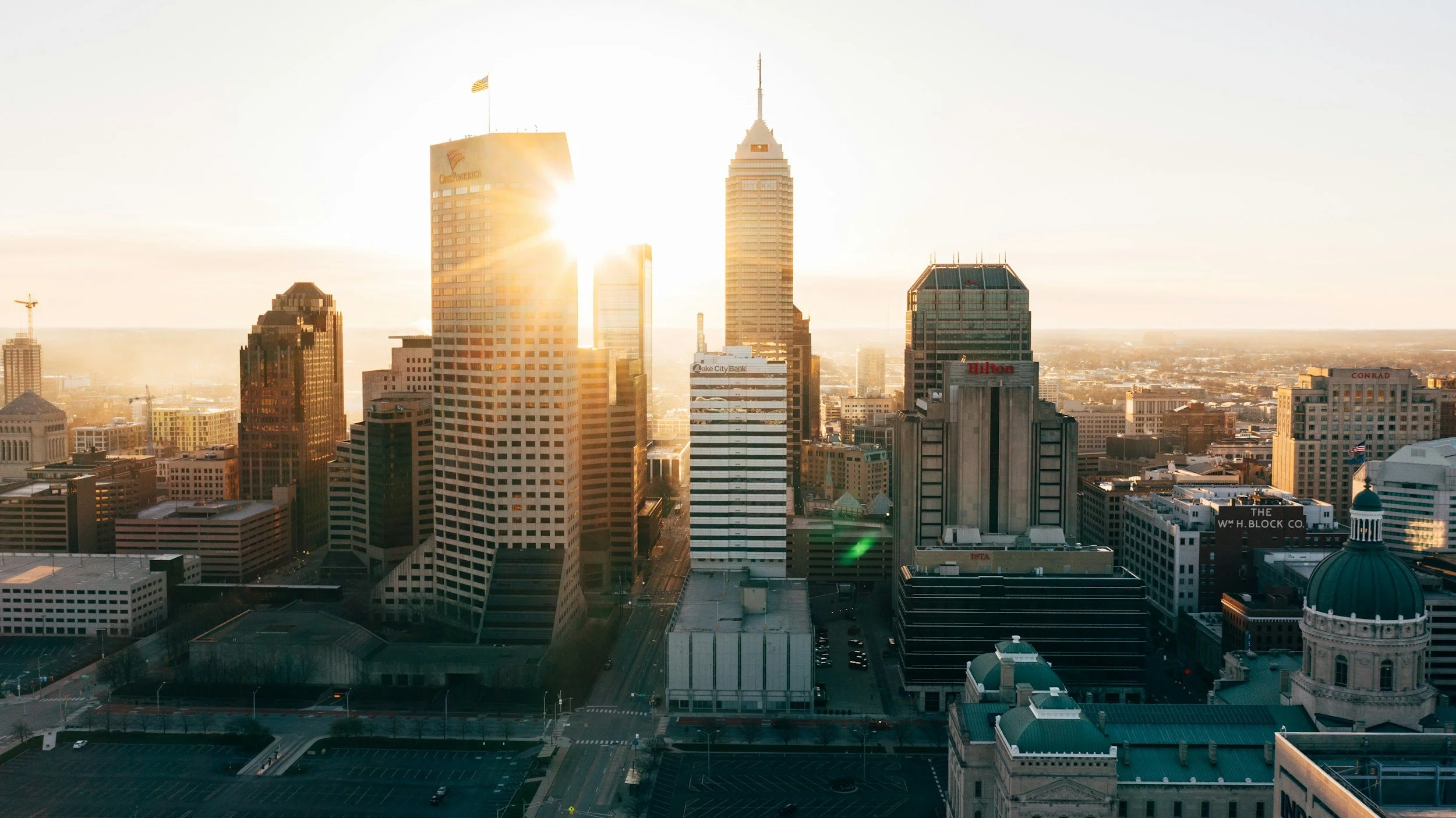 A city skyline at sunrise with tall skyscrapers, sunlight reflecting off the buildings, and the city stretching into the distance.