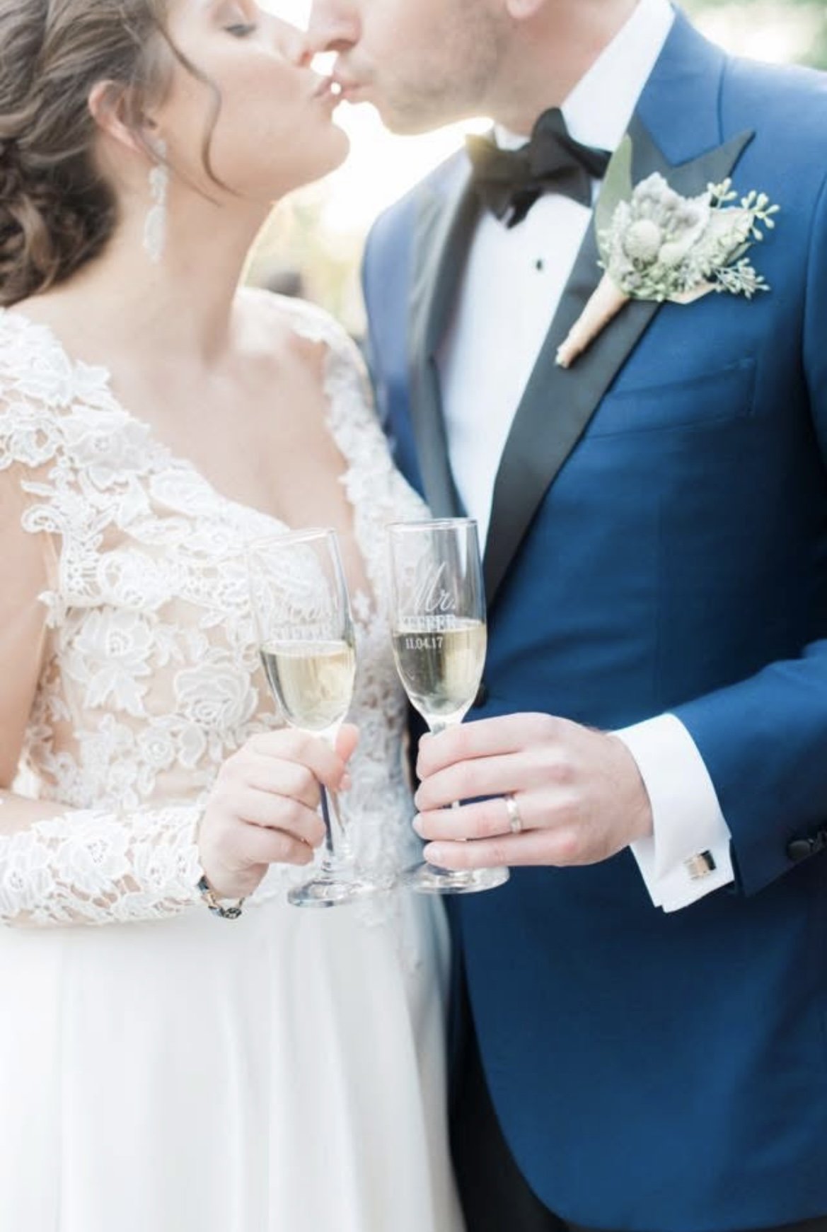 Bride and groom kissing while holding champagne glasses during wedding celebration.