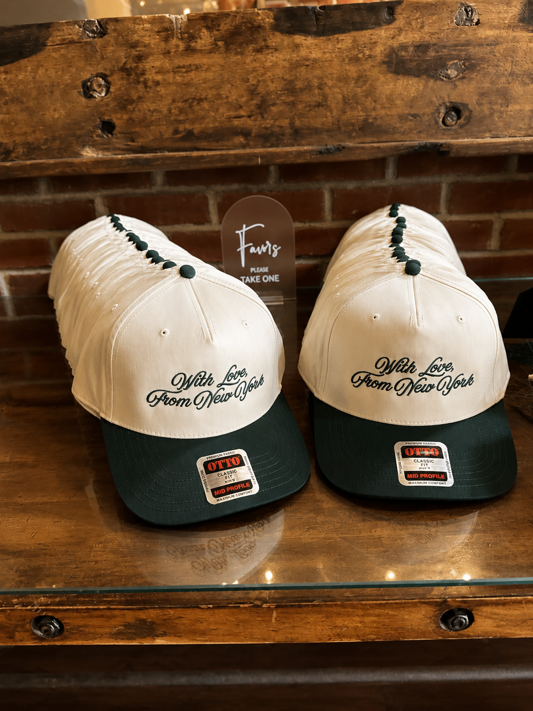 Several white and black baseball caps with the phrase 'With Love, From New York' embroidered on the front, displayed on a wooden surface.