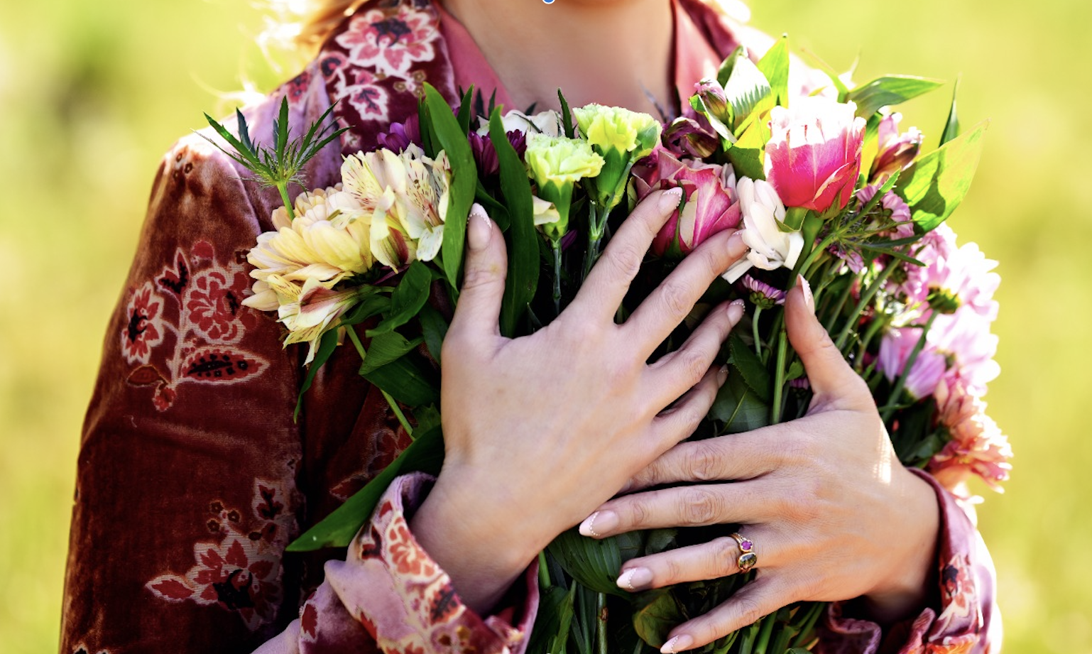Hands holding a colorful bouquet of wildflowers outdoors.