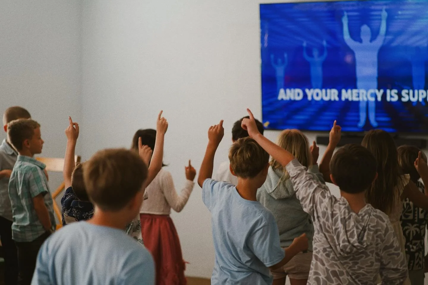 Children raising their hands in a classroom while watching a presentation on a big screen.
