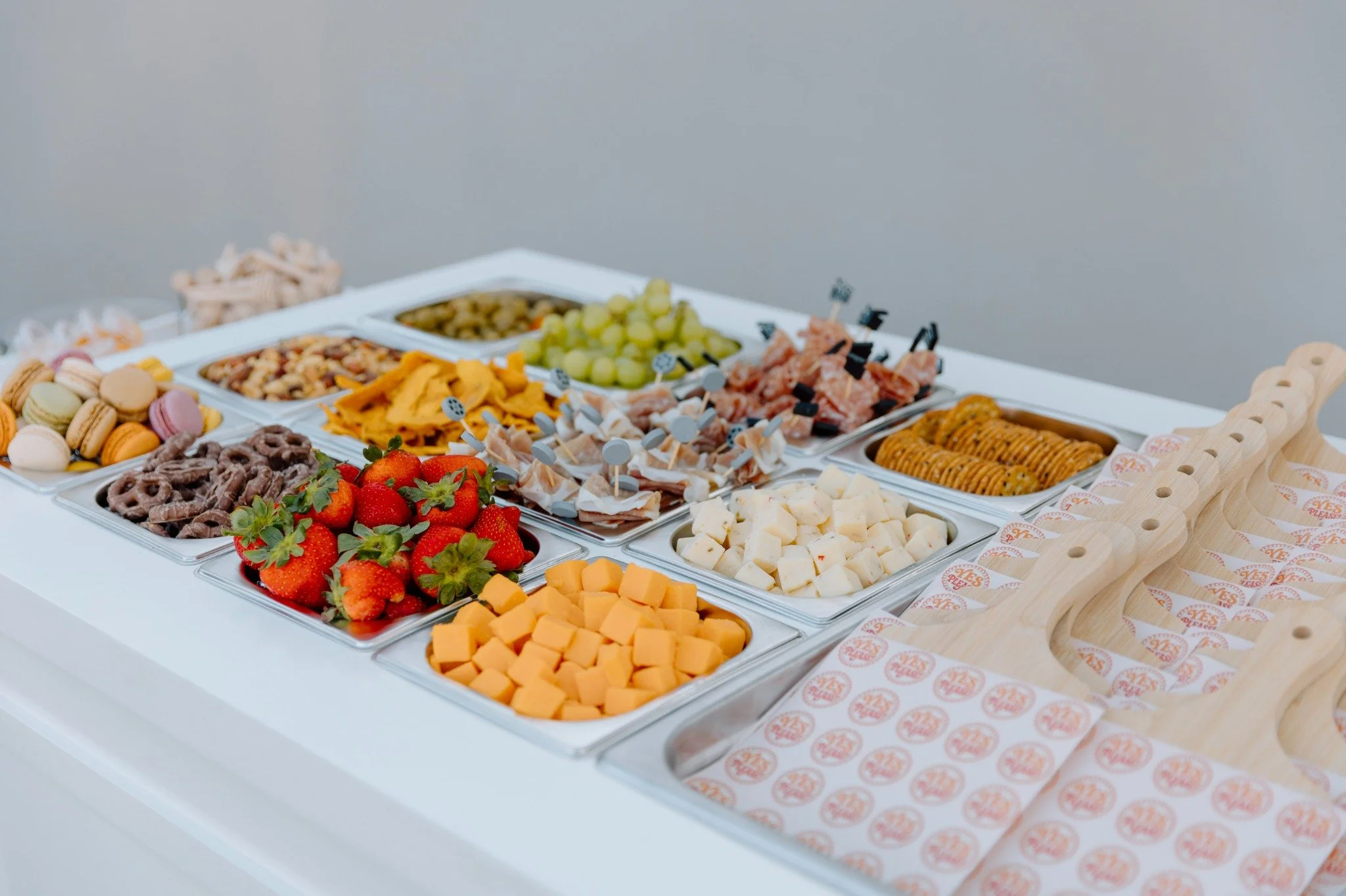 A cheese, fruit, and snack platter with strawberries, cubed cheese, macarons, and various dips and toppings on a white table.