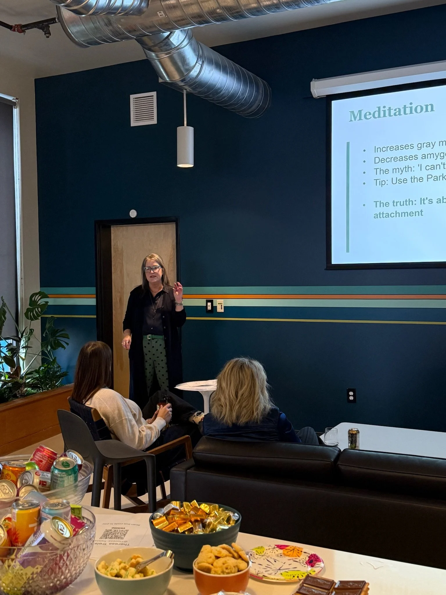 Theresa Trelstad giving a Reiki Share presentation for Reiki Attuned Practitioners coming together in community in a room with a projection screen displaying a slide titled 'Meditation'. Several attendees are seated and listening.