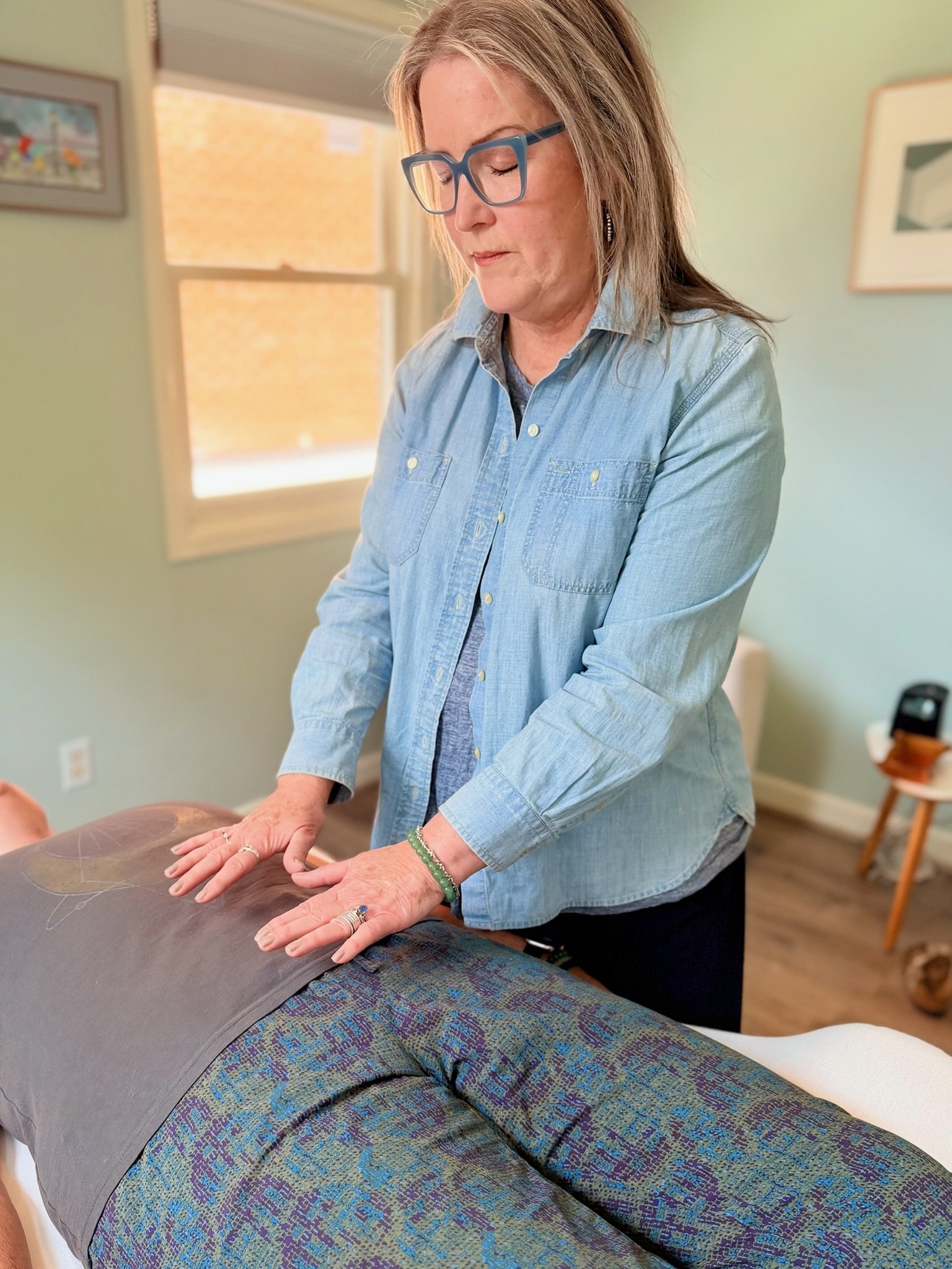 Theresa Trelstad performing Reiki Energy Healing Therapy on person lying on a massage table in a therapy room during an Individual Reiki Session.