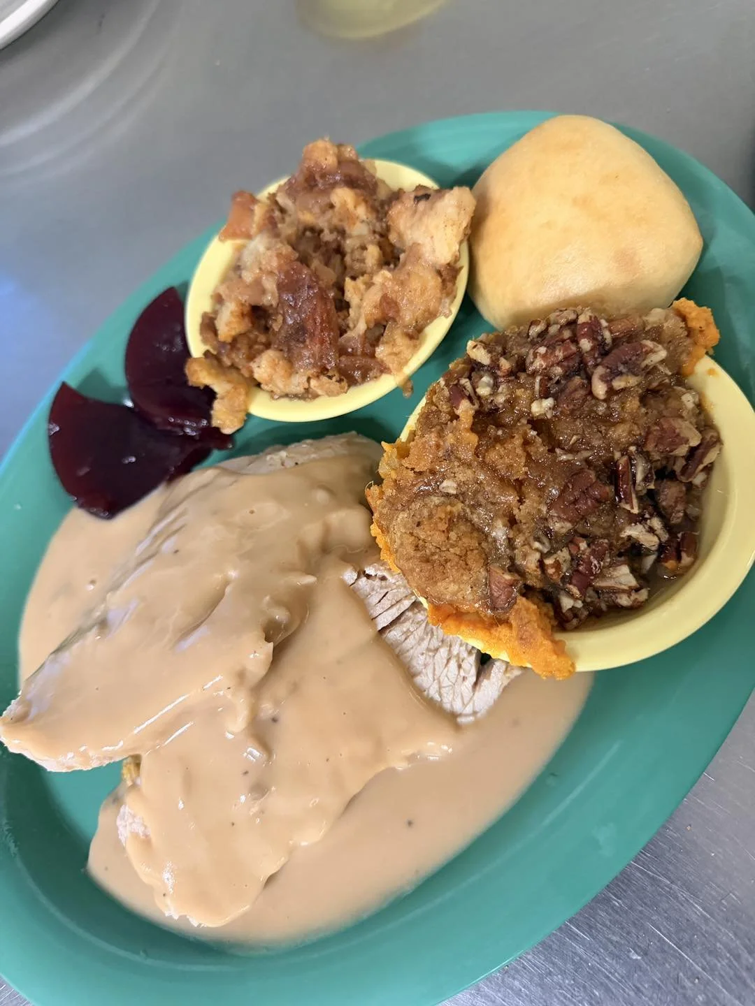 A plate of food with stuffing, turkey with gravy, a dinner roll, and cranberry sauce.