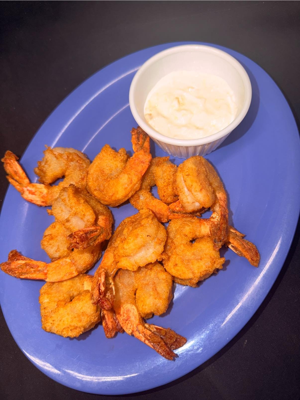 Fried shrimp served on a blue plate with a cup of dipping sauce on the side.
