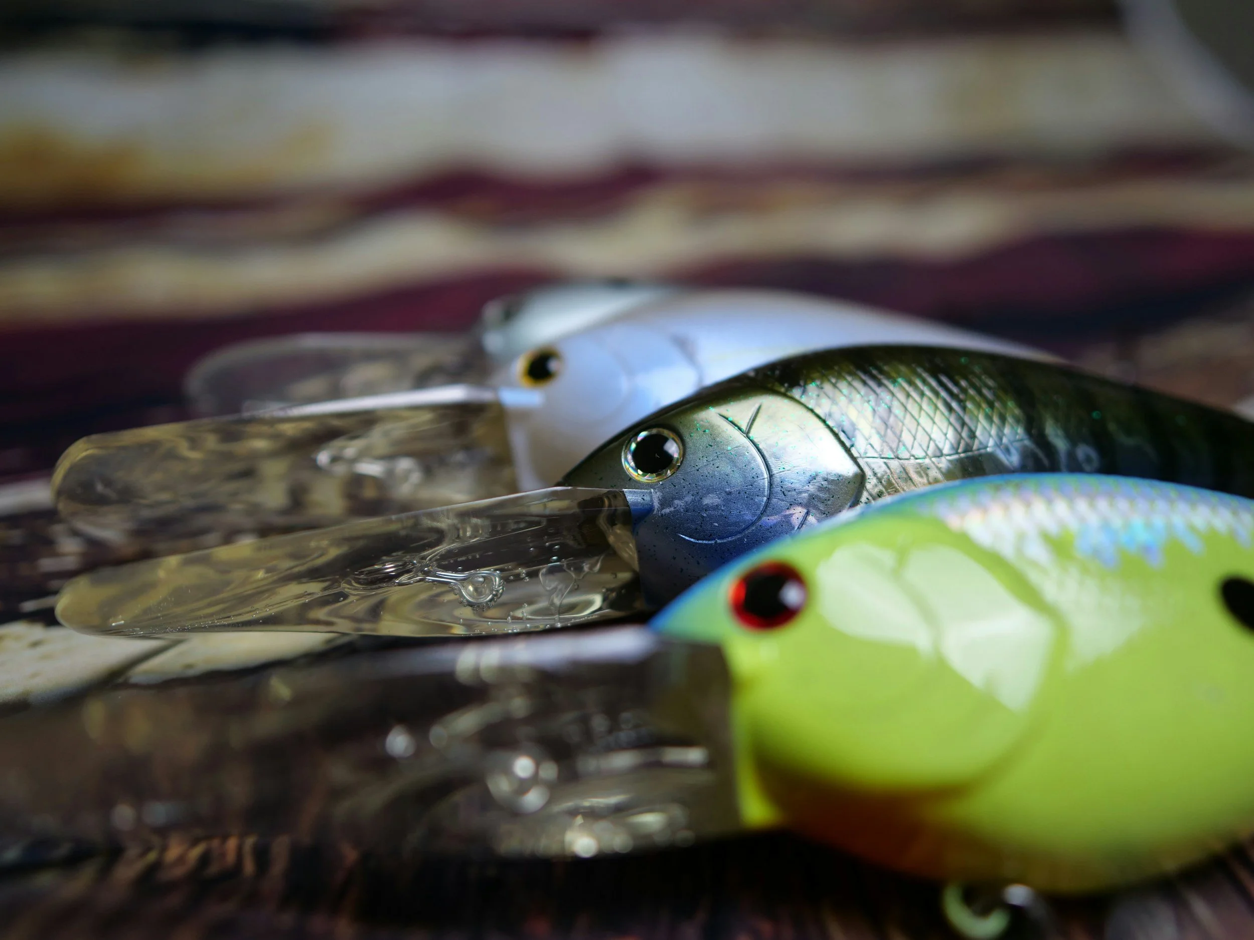 Close-up image of several fishing lures with shiny, reflective surfaces, some with colorful accents, laid out on a surface with a blurred background.