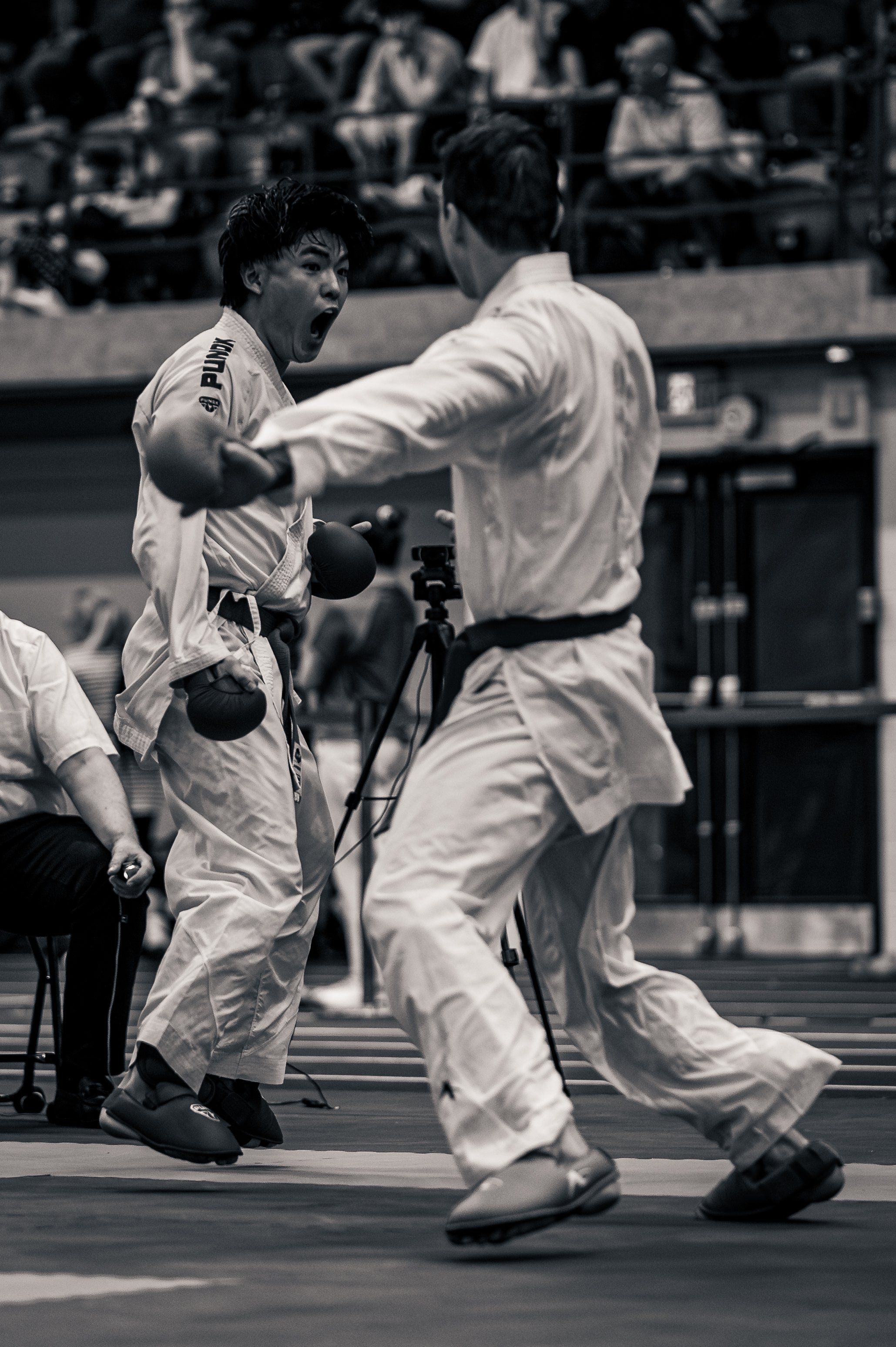 Two martial artists in white uniforms fighting at the montreal international open, with spectators in the background, in a black-and-white photograph.