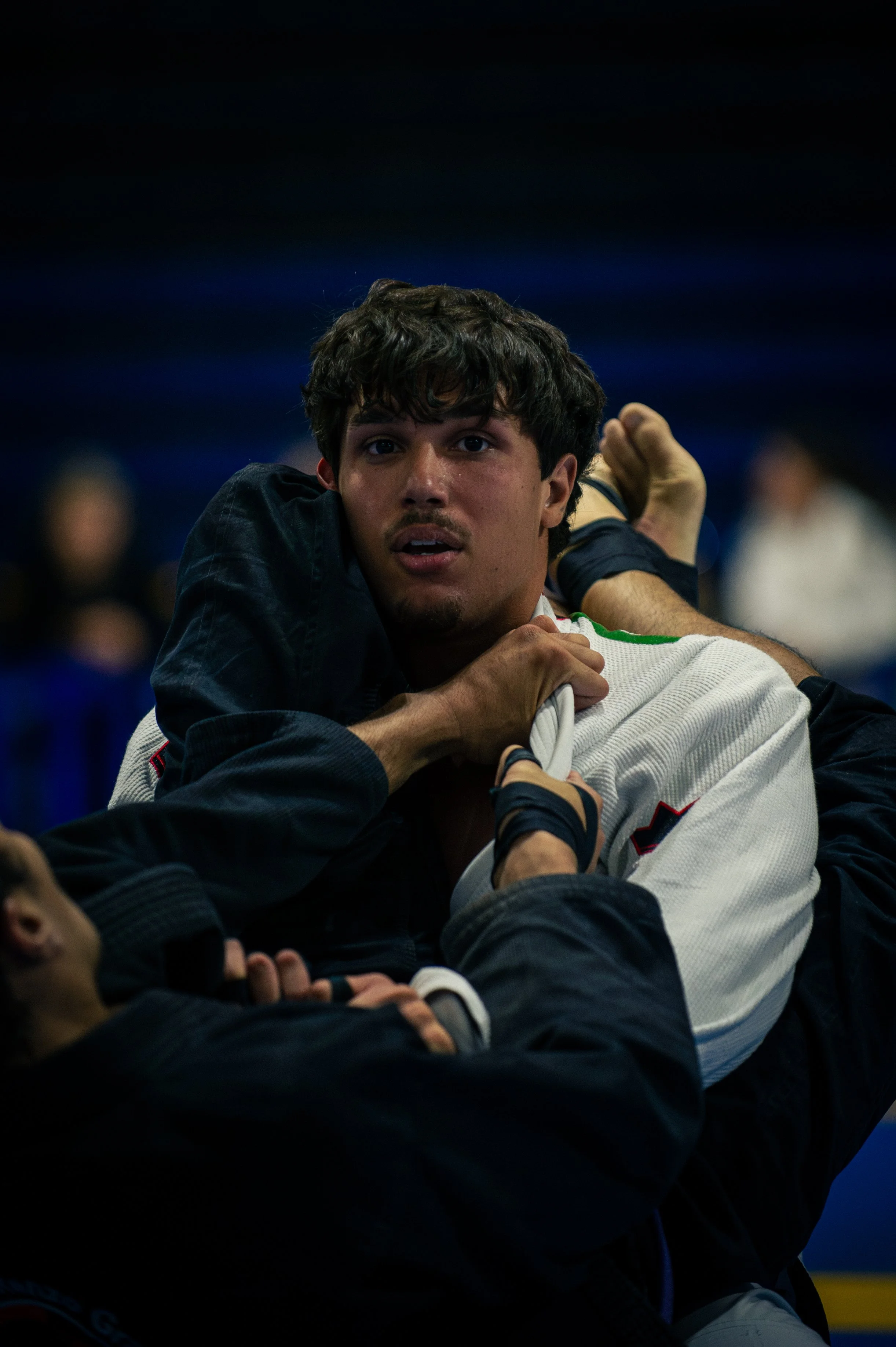 A male Brazilian Jiu-Jitsu competitor in a white gi, opponent in a black gi during a match.
