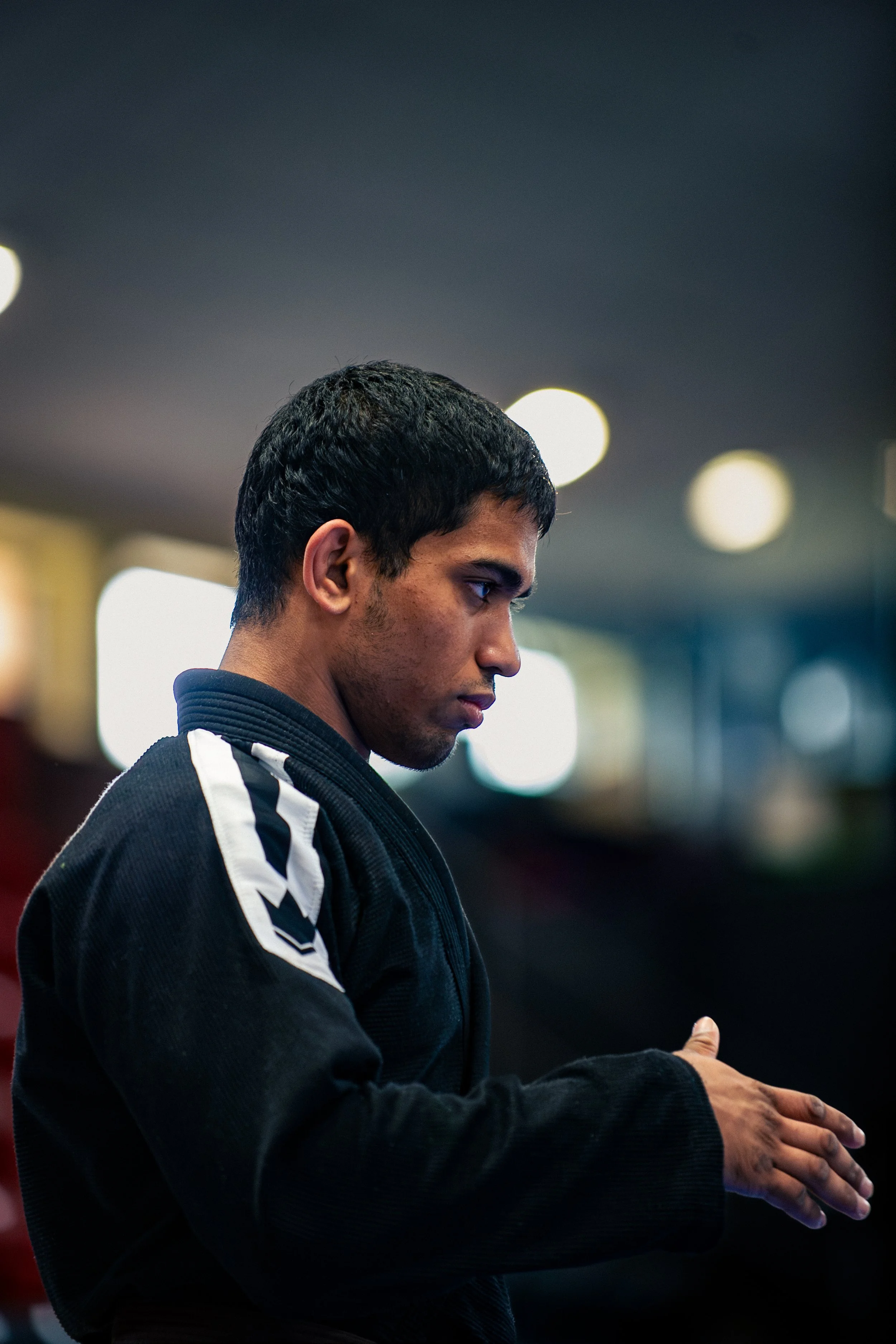 Young man in a black martial arts gi preparing in a competition environment, with a focused expression.