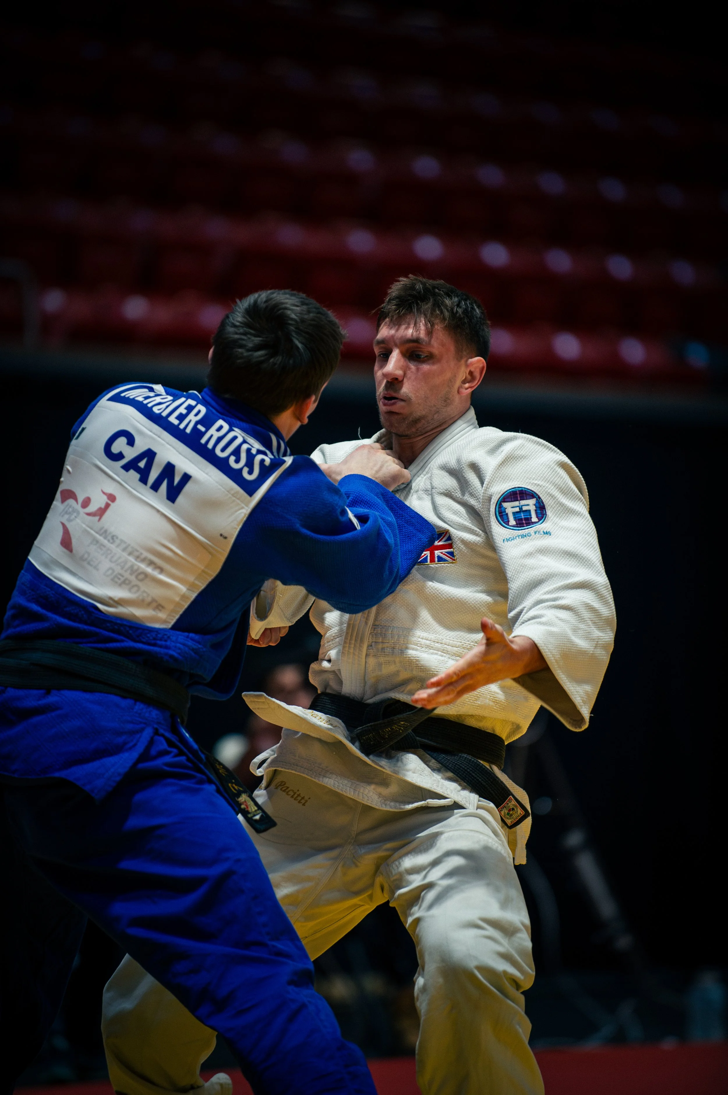 Two judo competitors engaged in a match, one in a blue gi and the other in a white gi, with the boxer in the white gi gripping the collar of the blue gi.