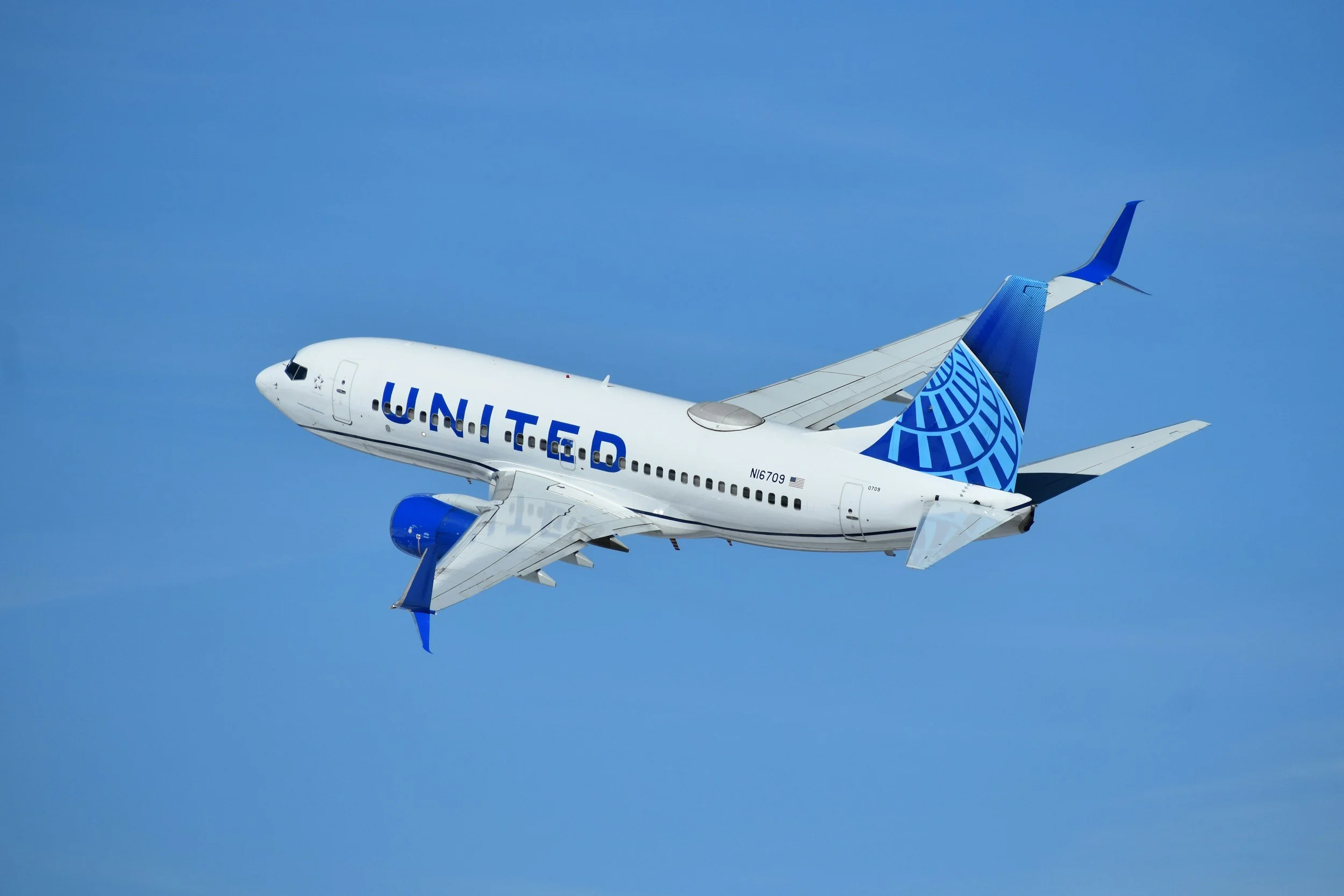 An United Airlines commercial airplane flying in a clear blue sky.