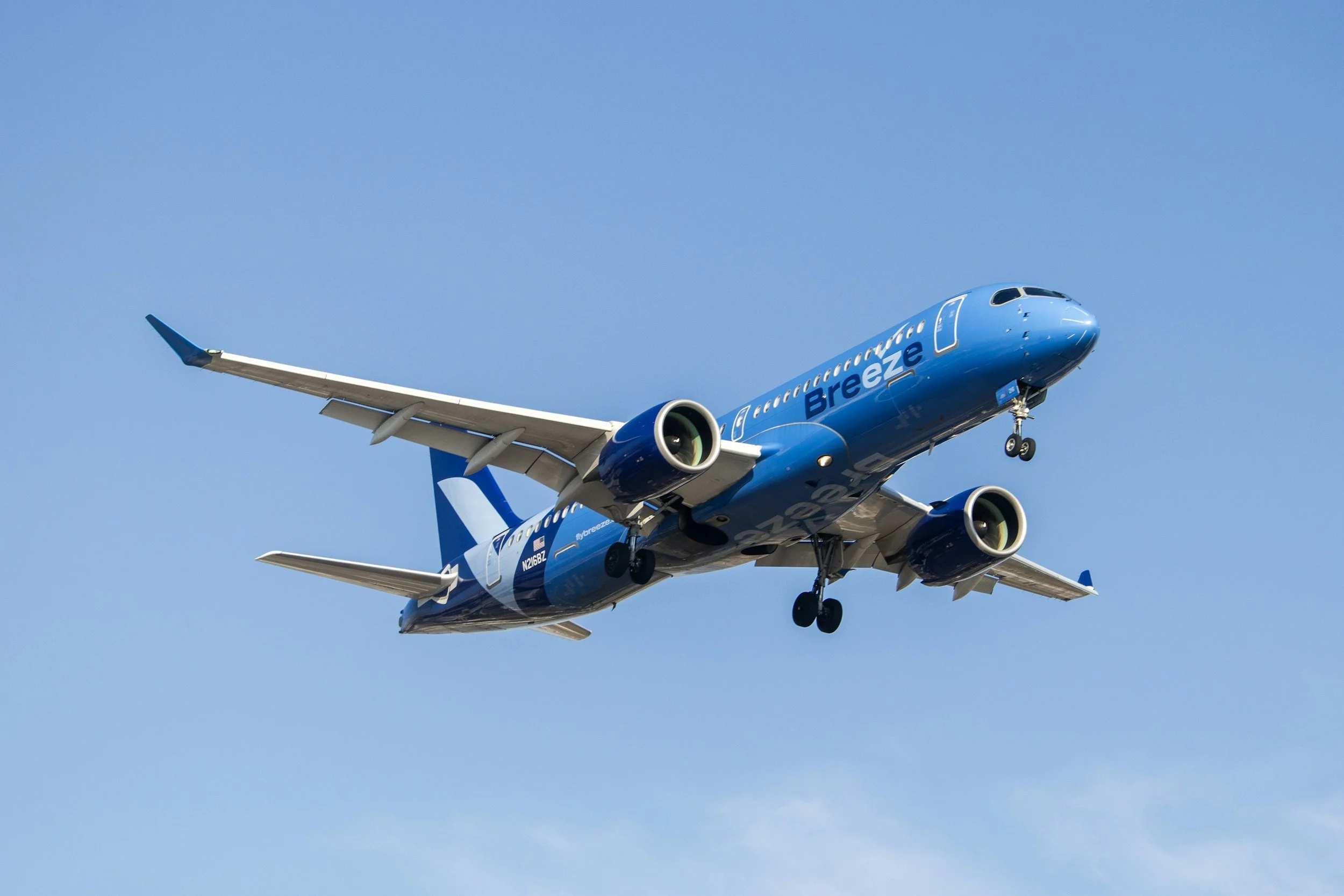 A blue Breeze airline airplane in flight against a clear blue sky.
