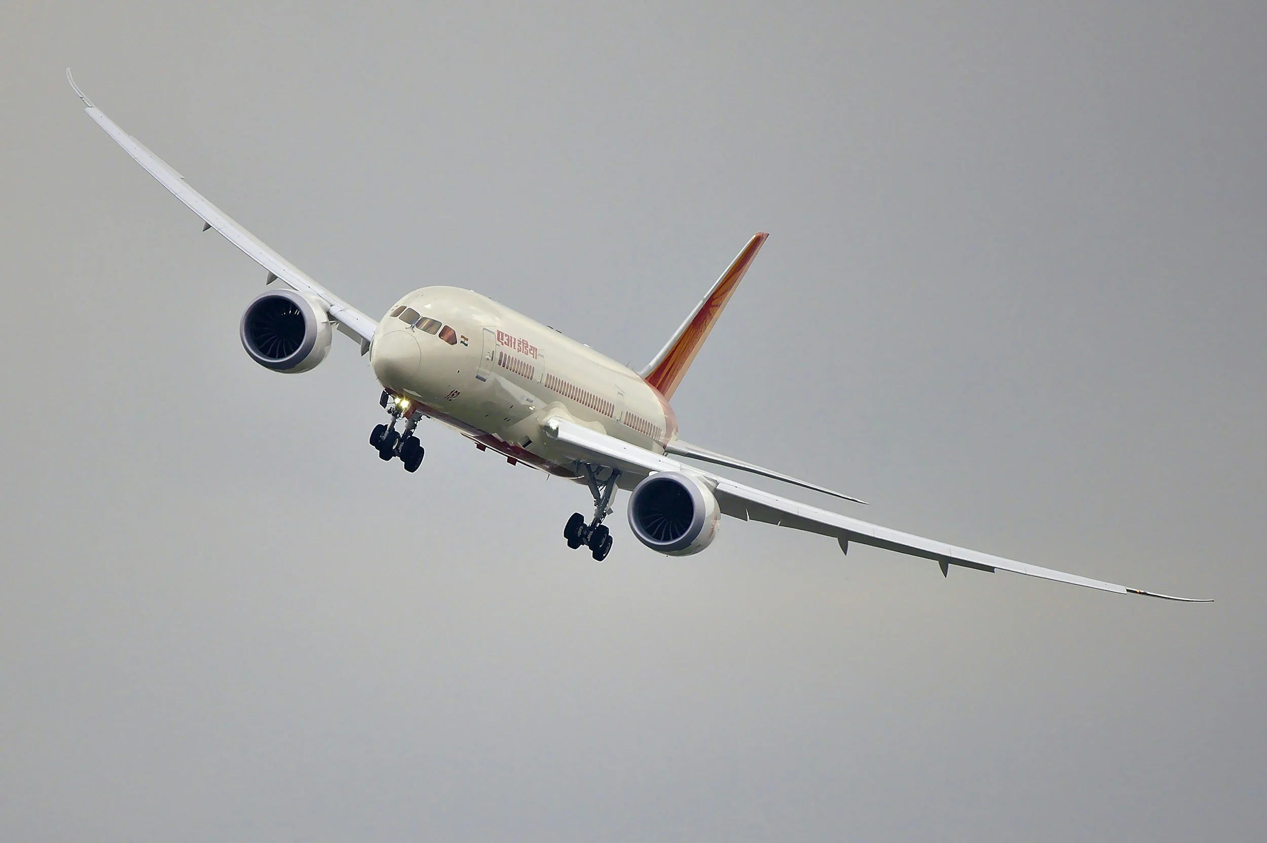 An airplane flying in a cloudy sky, viewed from below and slightly to the front.