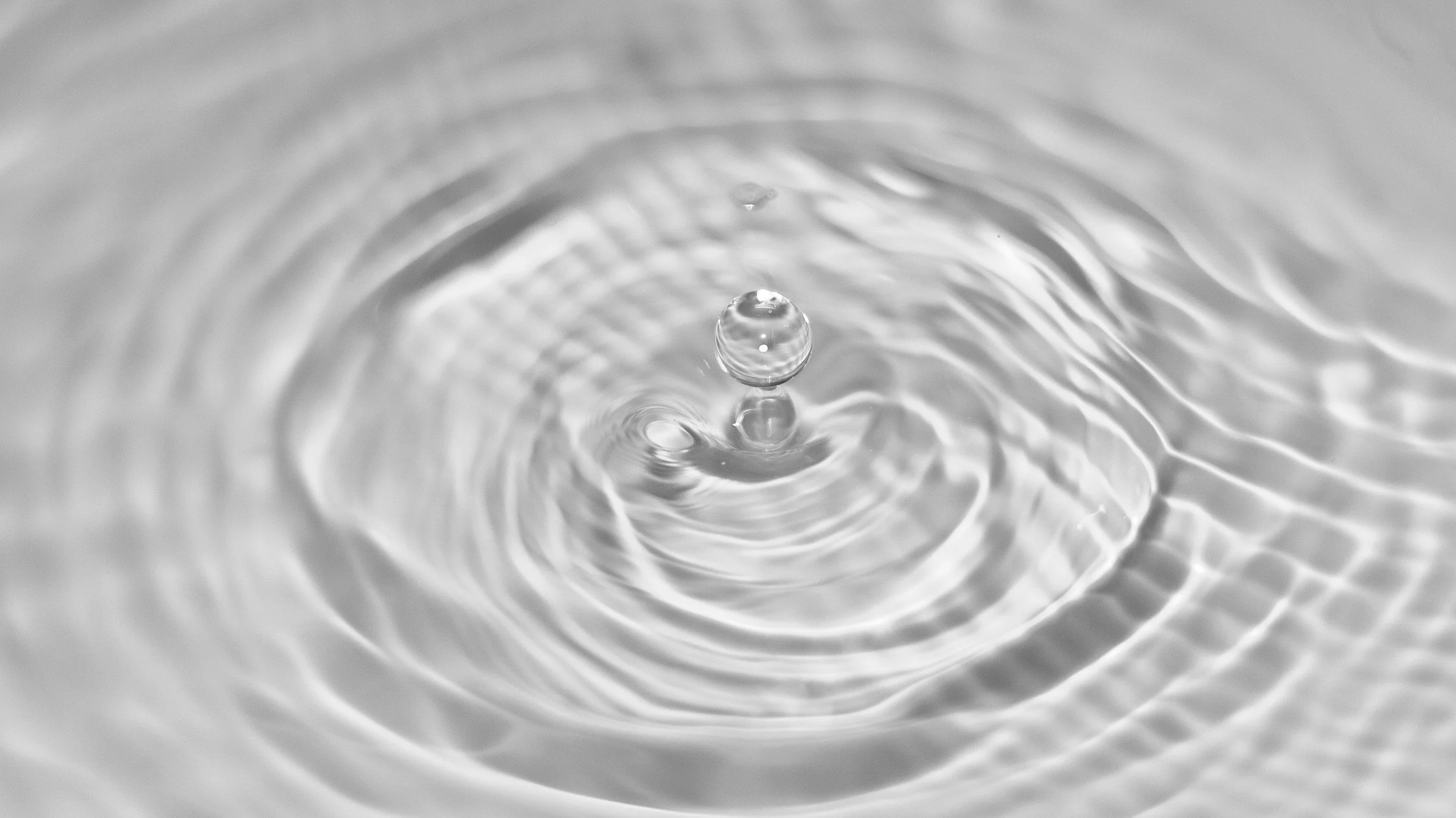 Close-up of a water droplet hitting the surface of water, creating ripples.
