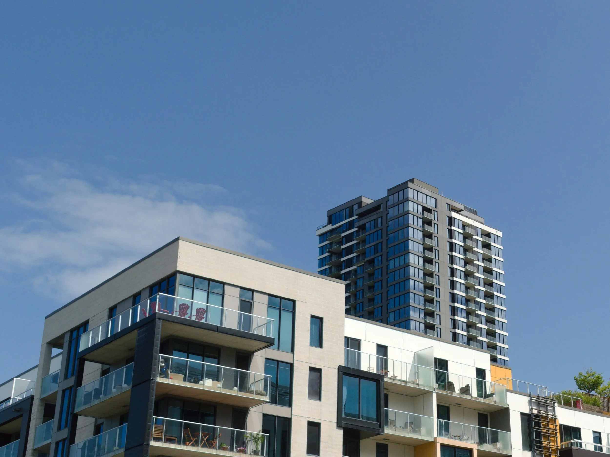 Modern multi-story apartment building with glass balconies set against a blue sky.