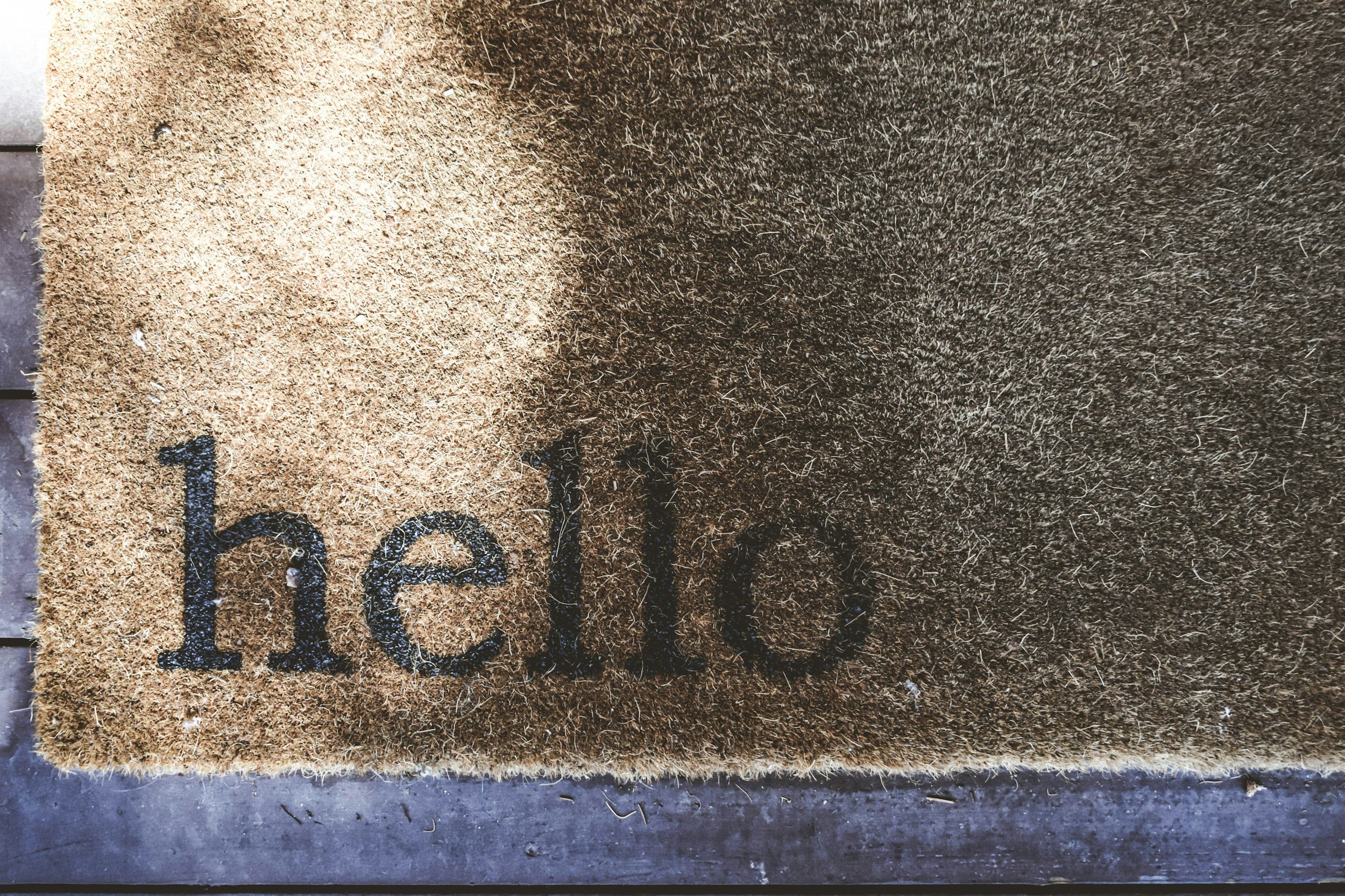 Close-up of a doormat with the word 'hello' written on it, placed on a concrete surface.