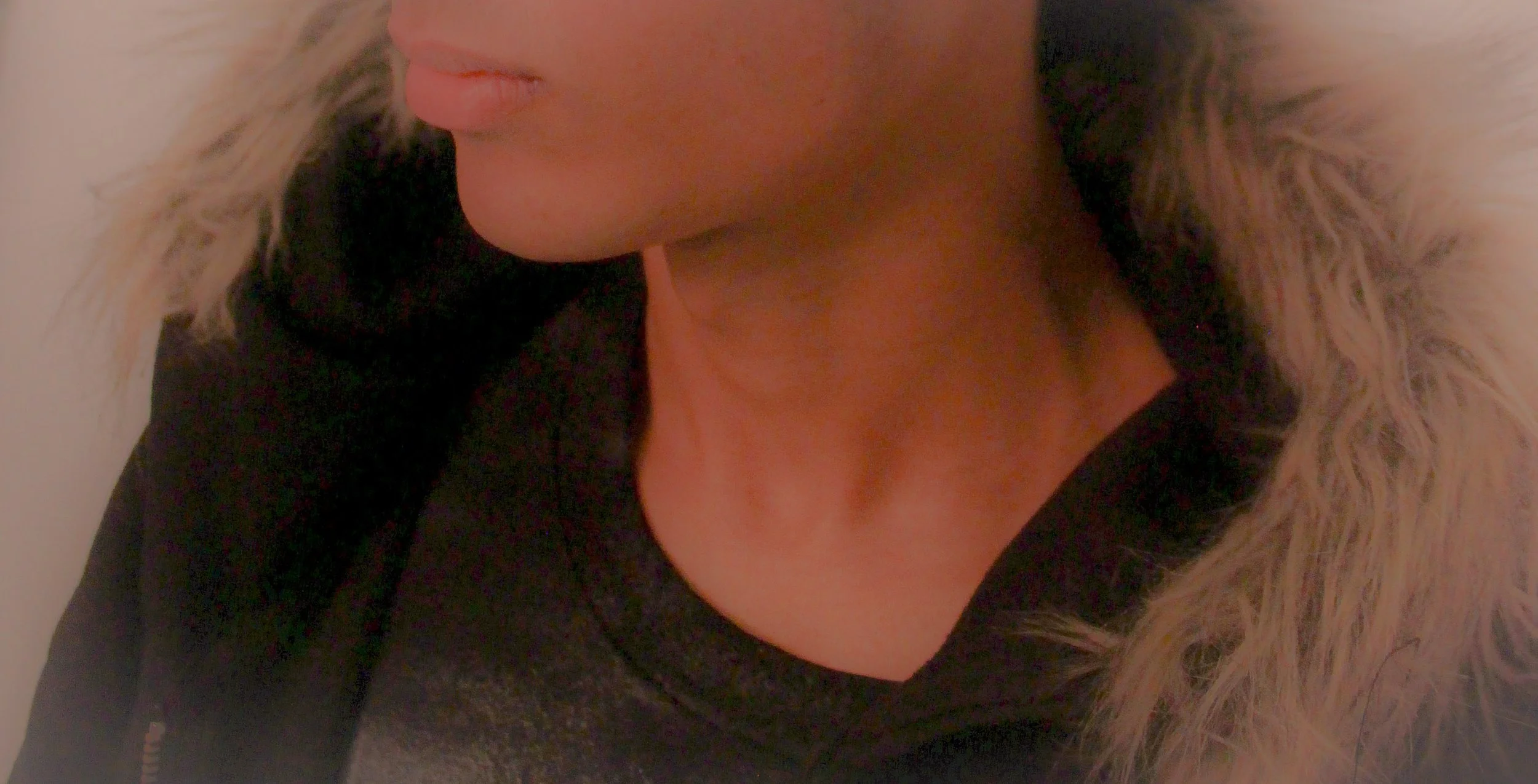 Close-up of a person's face with blonde hair and pink lips, partially covered with a fur-lined hood.