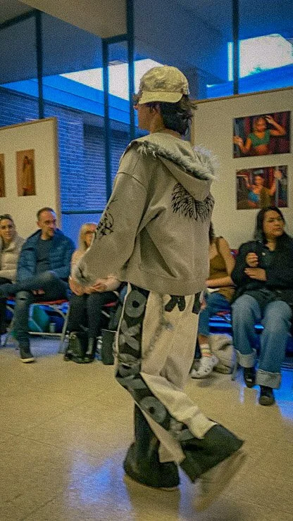 A person walking in front of seated audience members inside an art gallery or museum, with blue lighting and artwork on the walls.