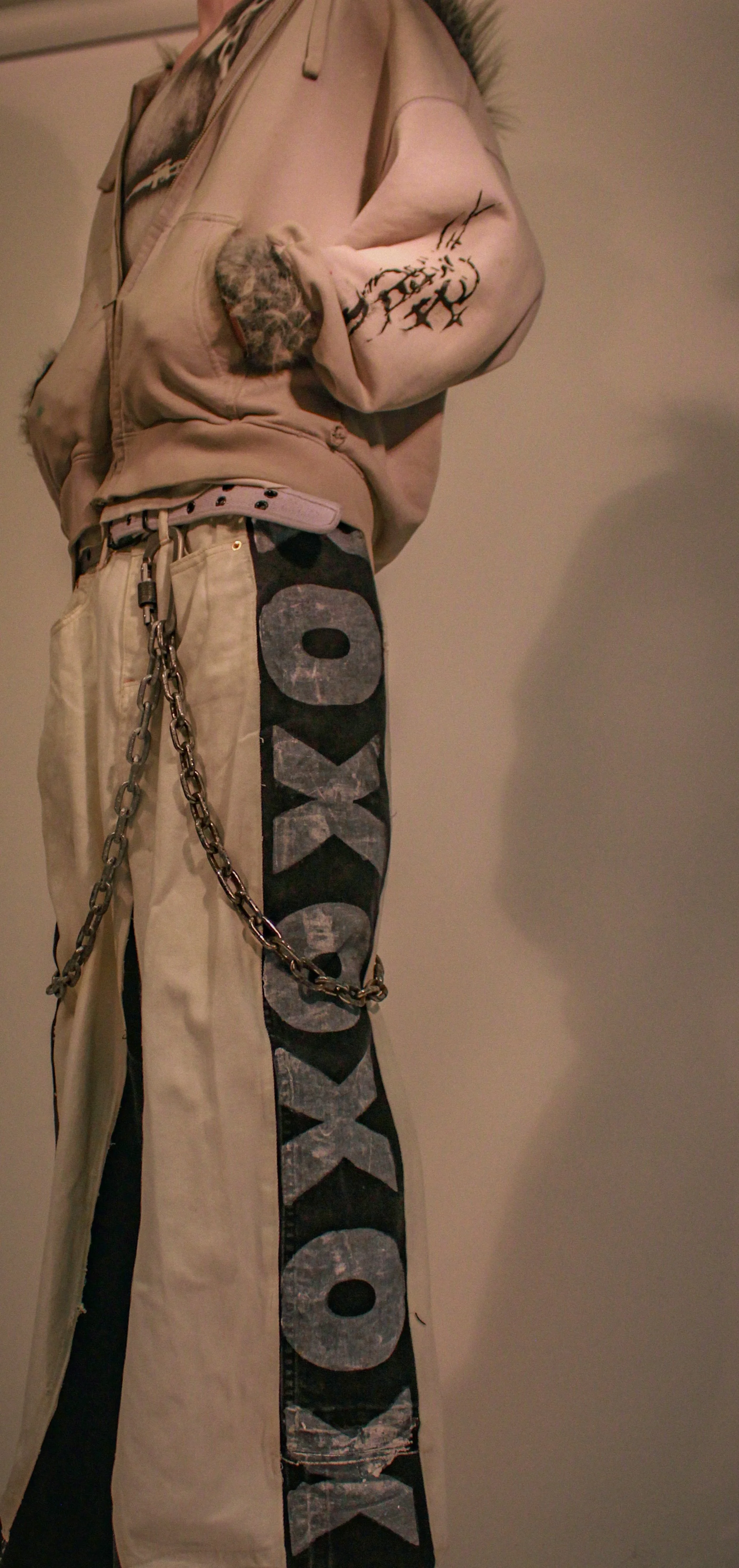 Part of a person dressed in beige and black denim clothing, with the word Coca-Cola on the black pants and a chain attached to the pants.