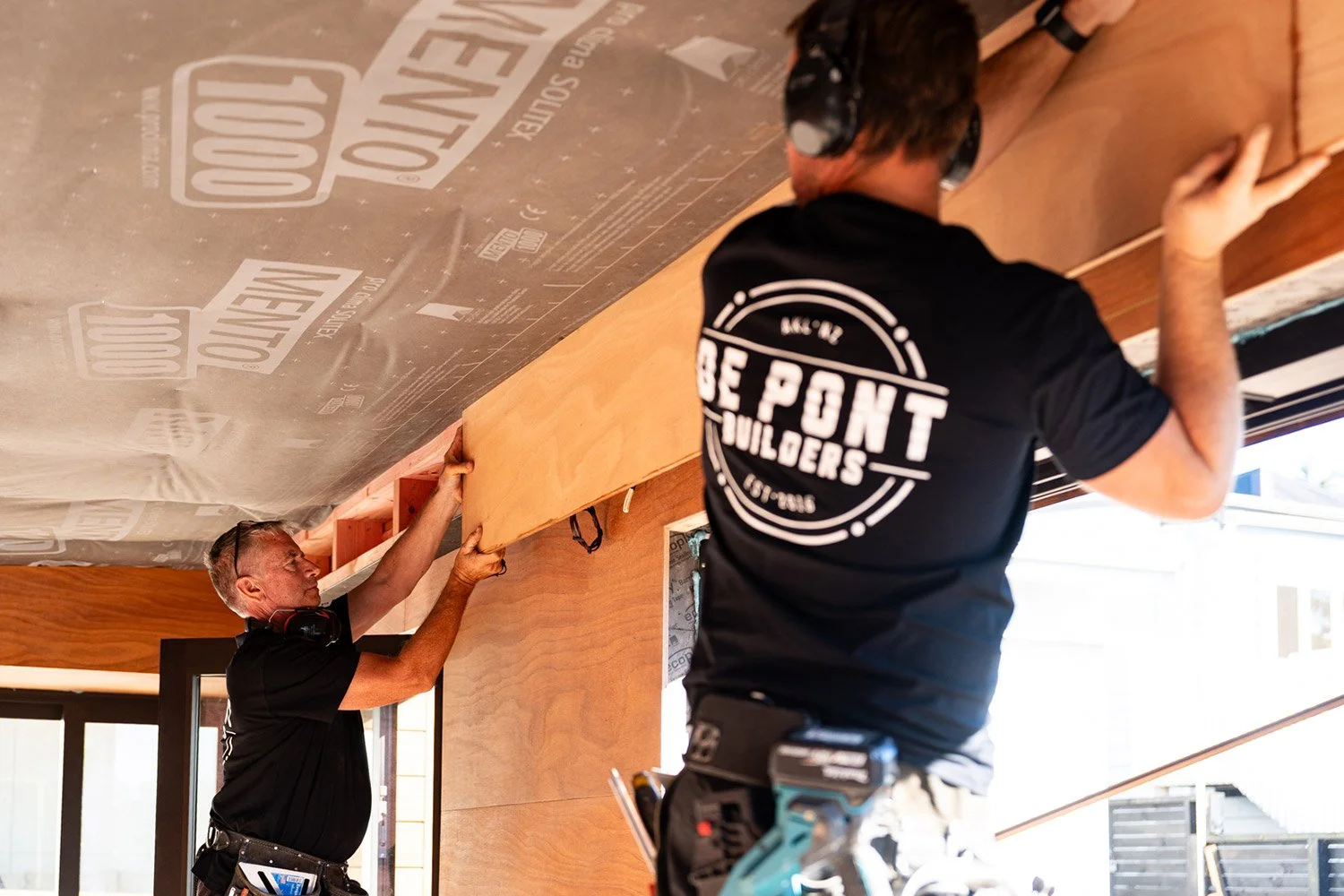 Two De Pont Builders construction workers installing a wooden beam inside a residential home being renovated in Auckland.