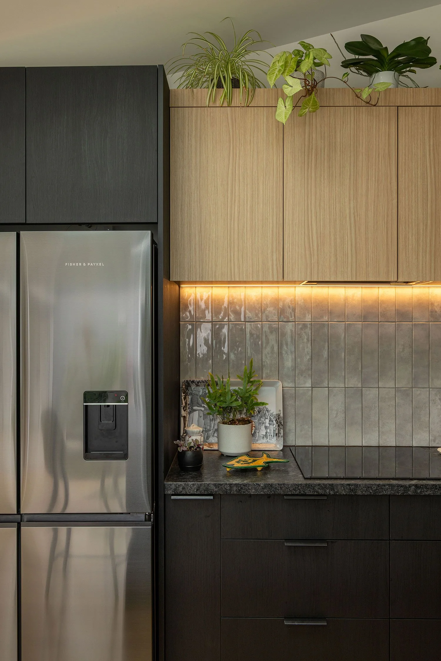 Modern renovated kitchen extension in Auckland with modern appliances and decor. On the left is a stainless-steel Fisher & Paykel refrigerator. The background includes wooden upper cabinets and a black granite countertop.