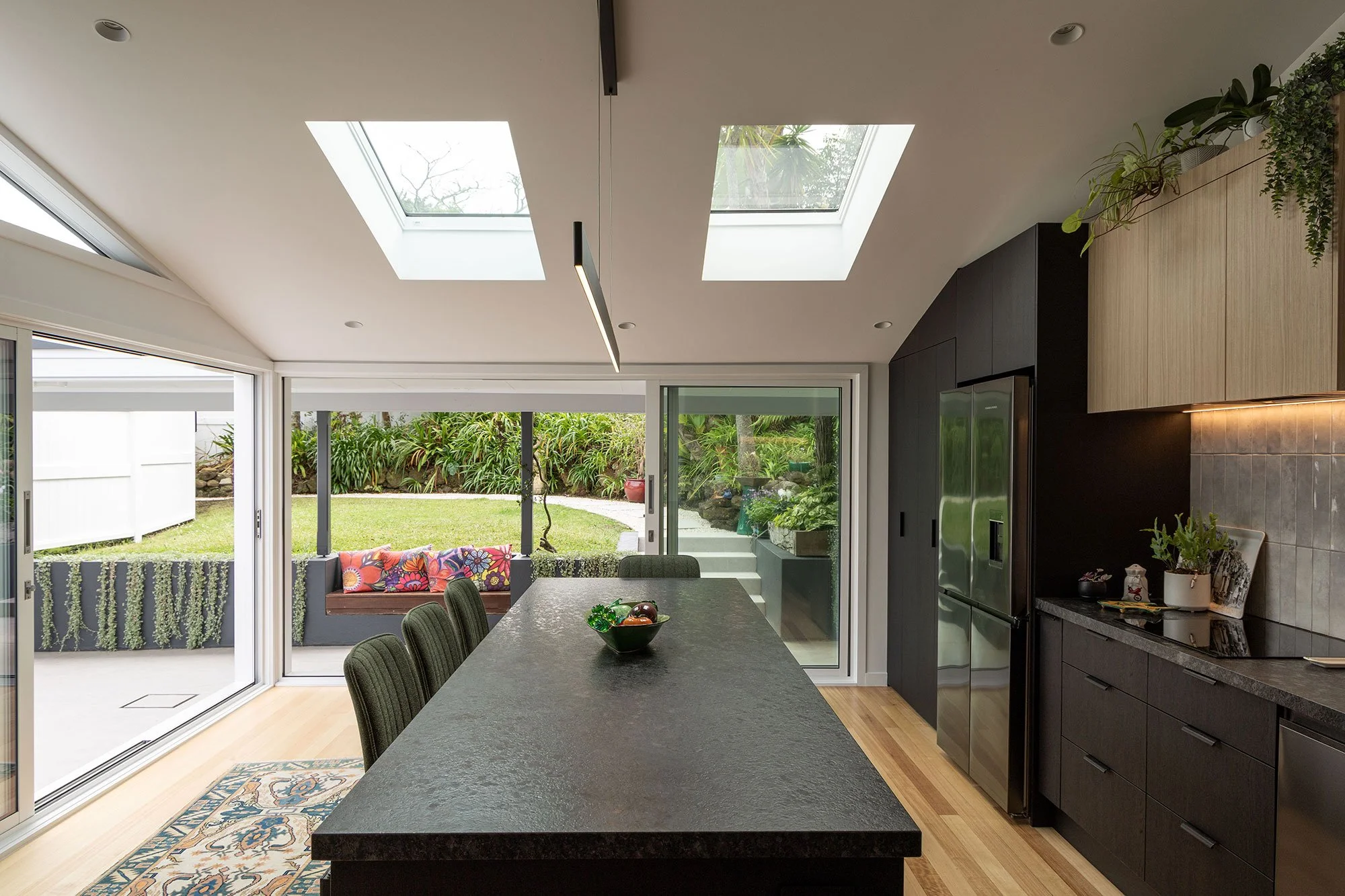 Open-plan renovated kitchen extension in Auckland with large skylights and sliding glass doors to the backyard, showcasing indoor-outdoor flow.