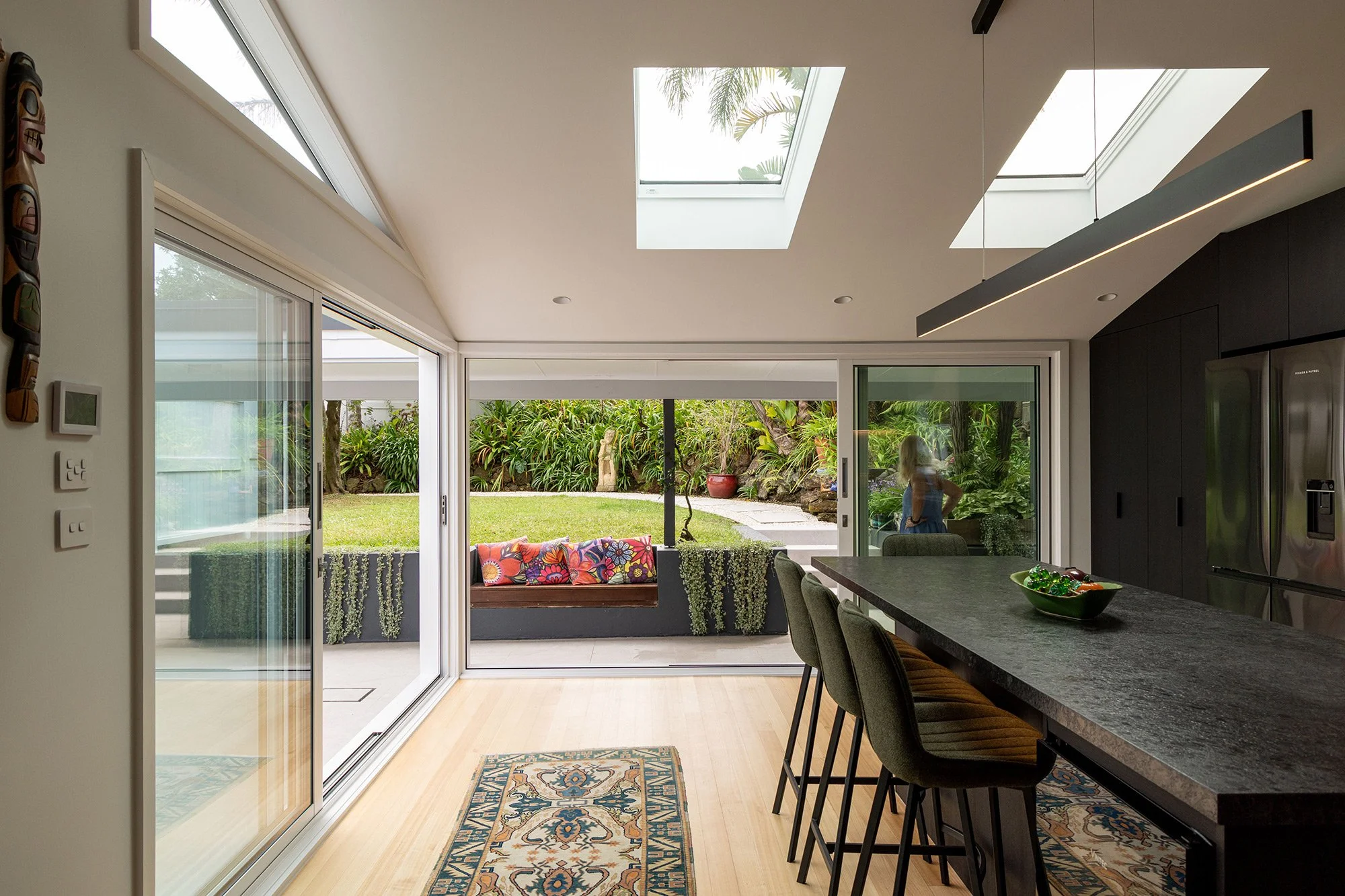 Open-plan renovated kitchen extension in Auckland with large skylights and sliding glass doors to the backyard, showcasing indoor-outdoor flow.