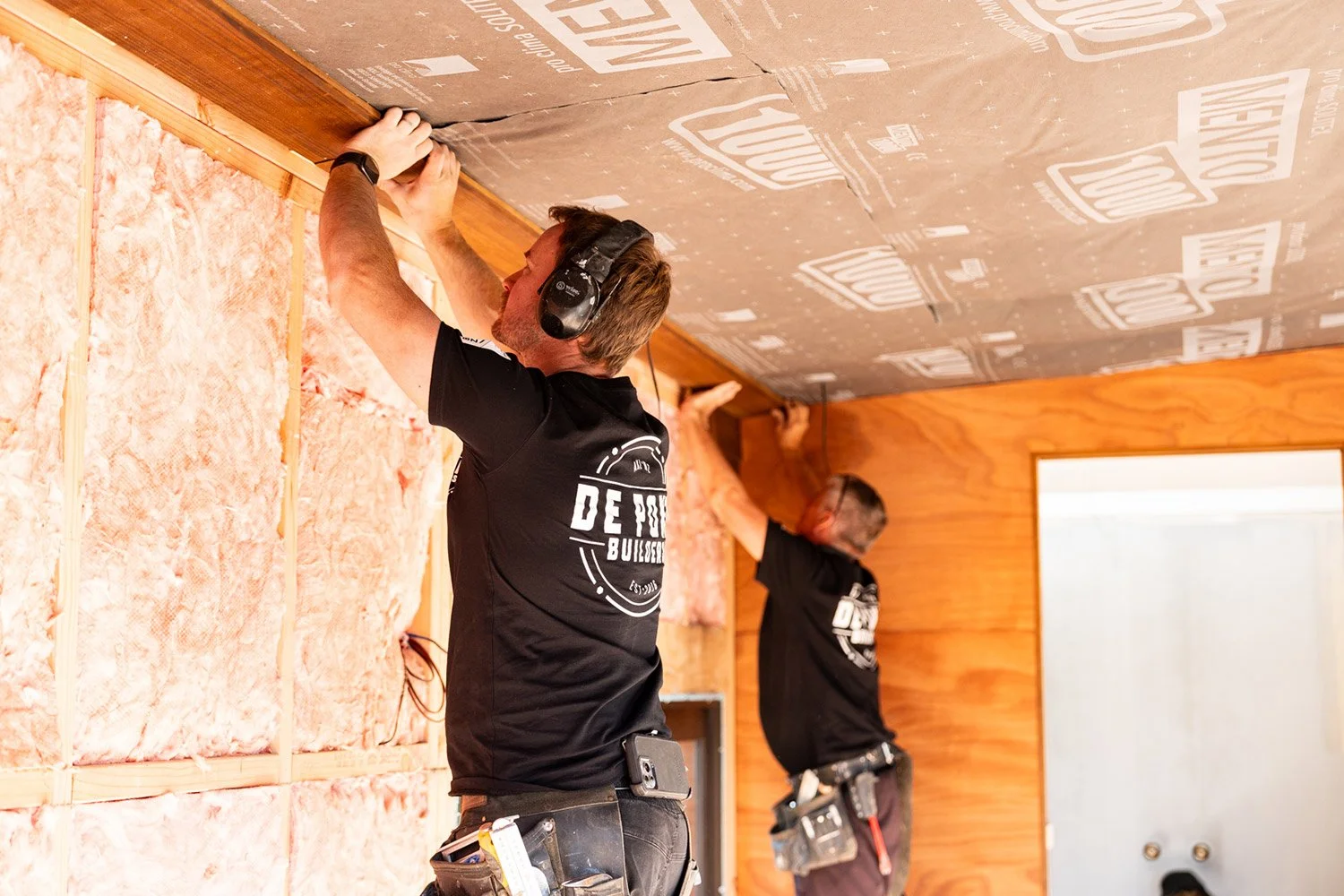 Two De Pont Builders' staff installing insulation in a wall of a room in Auckland showing attention to detail.