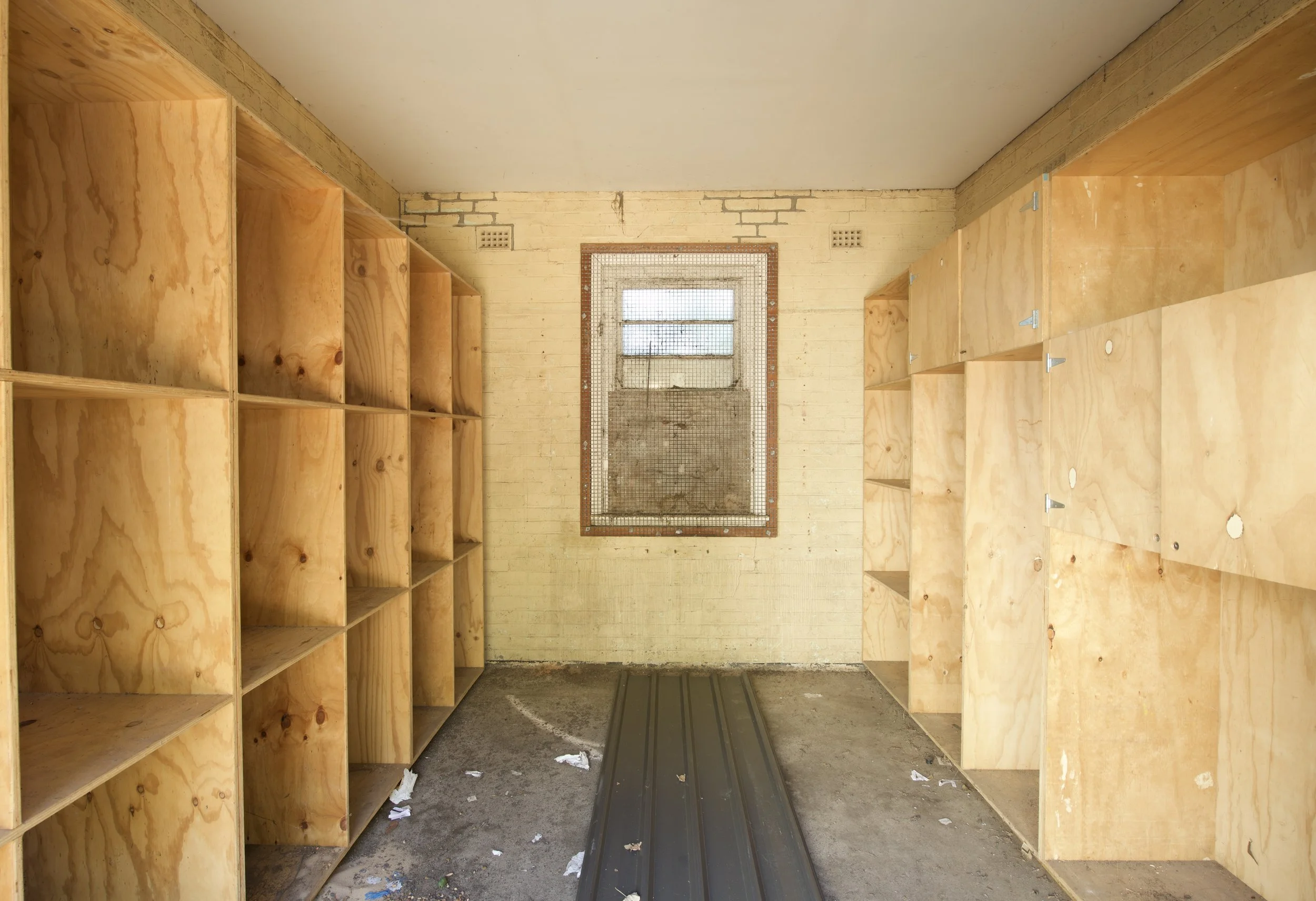 A partially constructed room with wooden shelves on both sides and a window at the back. The walls are painted yellow and there is debris on the floor.