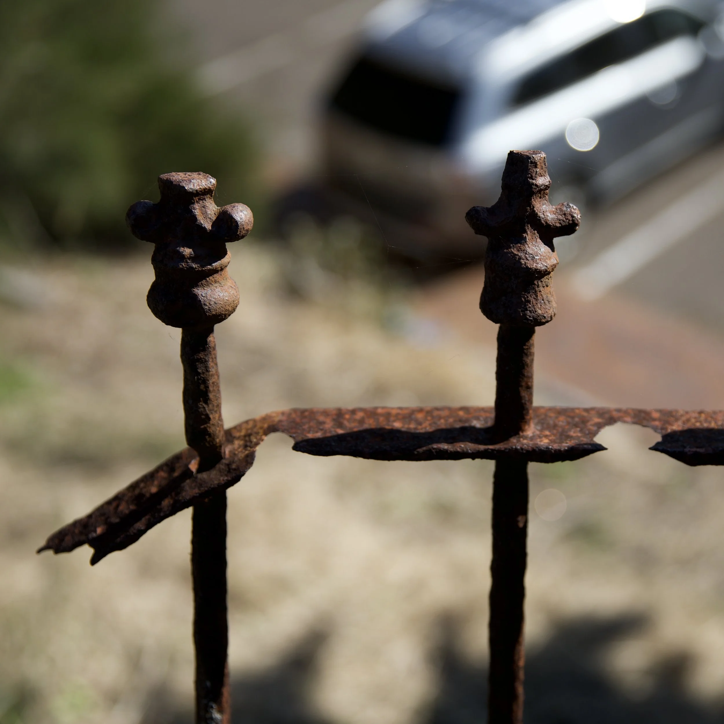 Close-up of rusted iron fence pickets with a blurred car in the background.