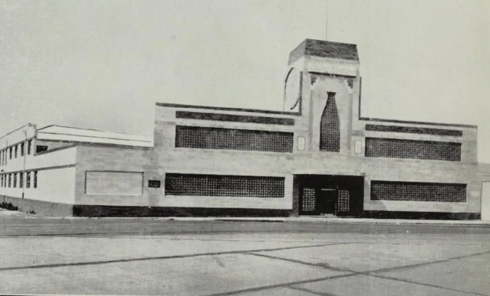 Black and white photo of a modern building with horizontal design, featuring large horizontal windows and a central tower with a bottle-shaped window.
