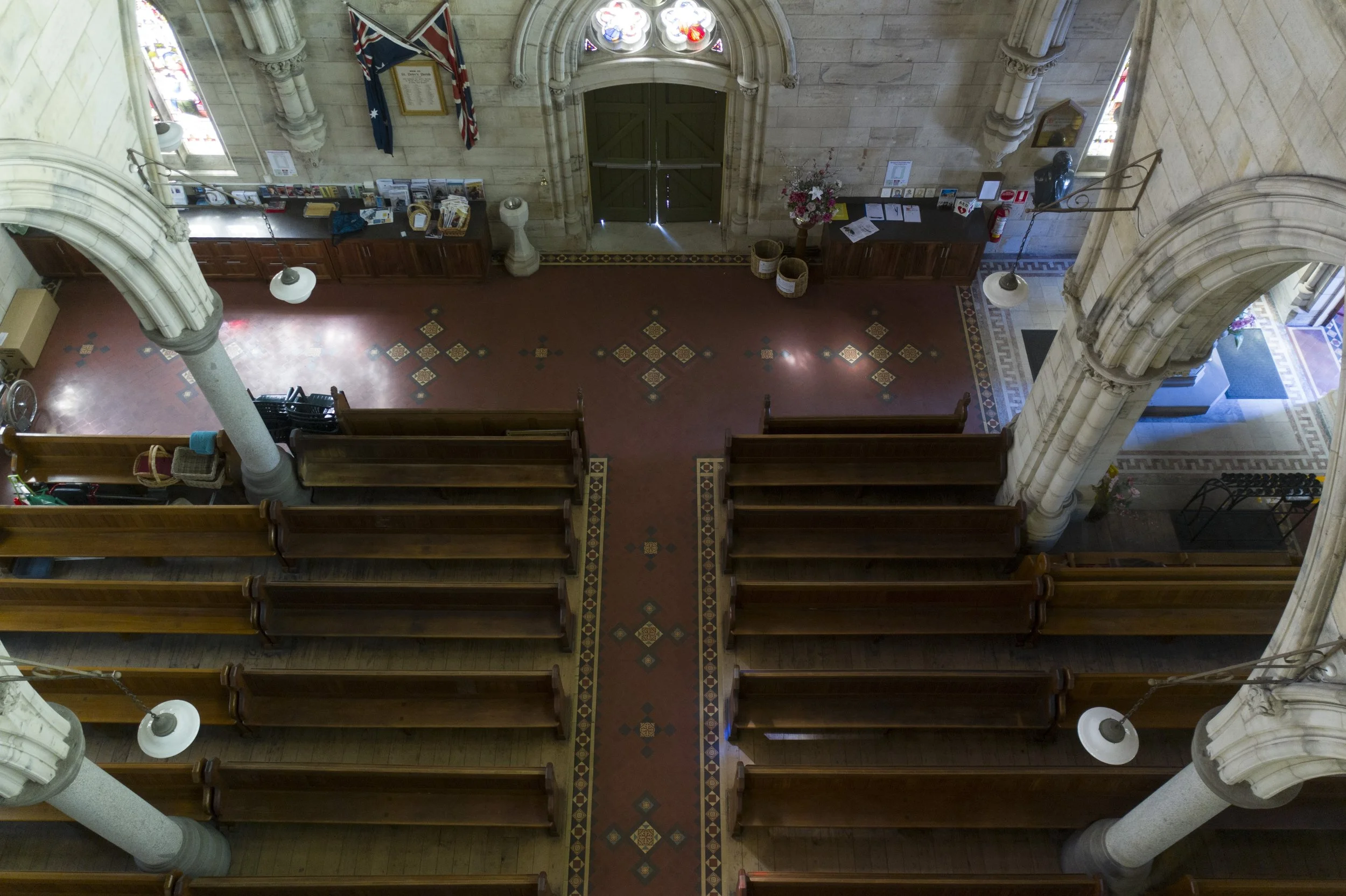Interior view of a church with wooden pews, large stone columns, ornate arches, and stained glass windows. There are flags hanging near the door and some books and informational materials on tables.