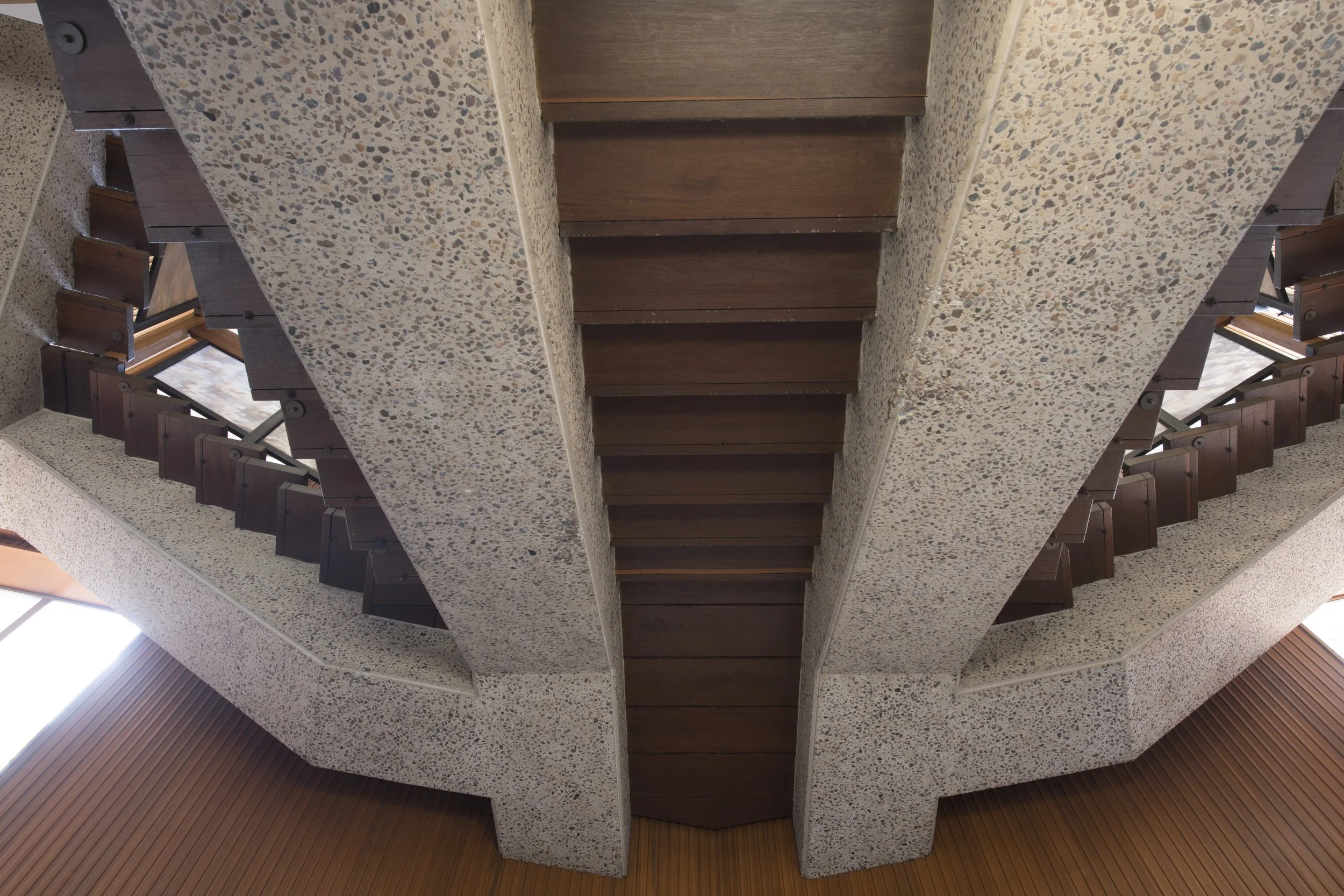 A spiral staircase with wooden steps and a speckled concrete railing, viewed from below.