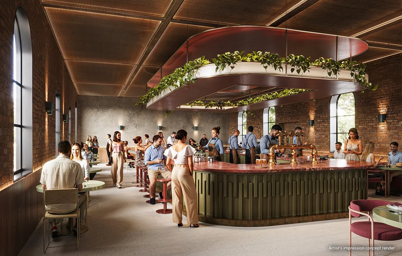 Interior of a modern restaurant or bar with brick walls, large arched windows, and a circular bar area with copper fixtures. People are seated and standing, enjoying drinks and conversation, with servers attending to customers. A large ceiling fixtur