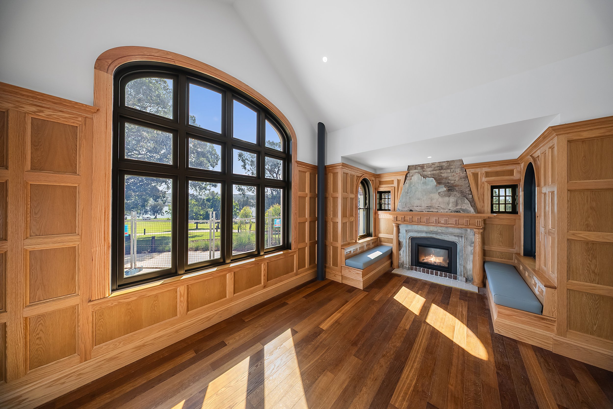 Living room with large arched window, wood paneling, stone fireplace, and built-in seating area.