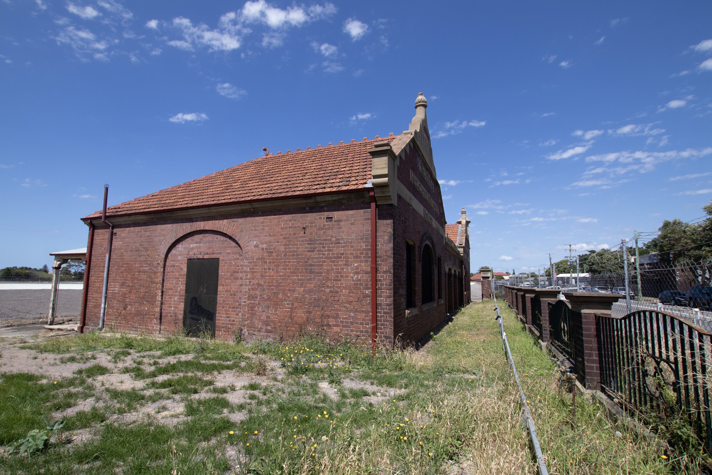 A brick building with a red tiled roof under a bright blue sky with small white clouds.