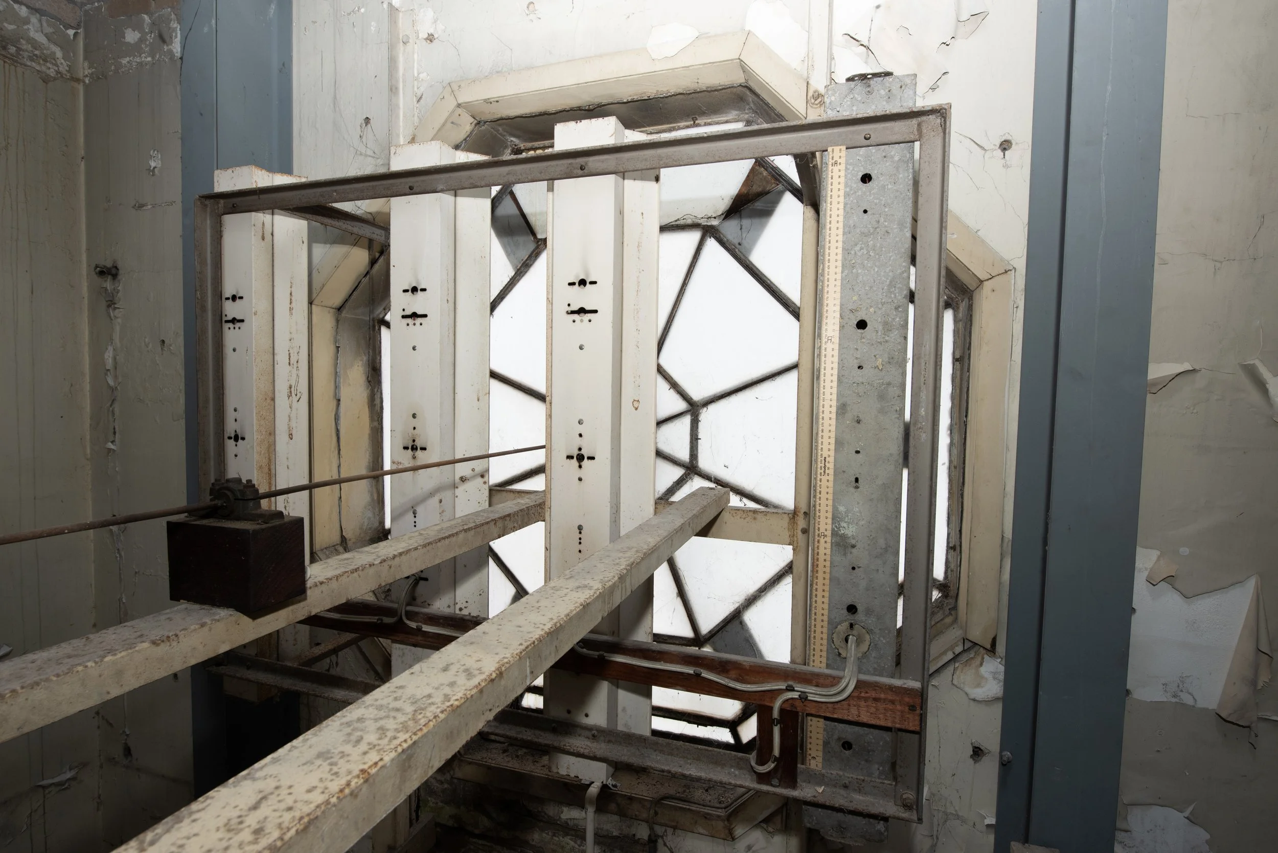View of an old elevator shaft with rusted metal beams, a pulley system, and cracked, peeling walls.