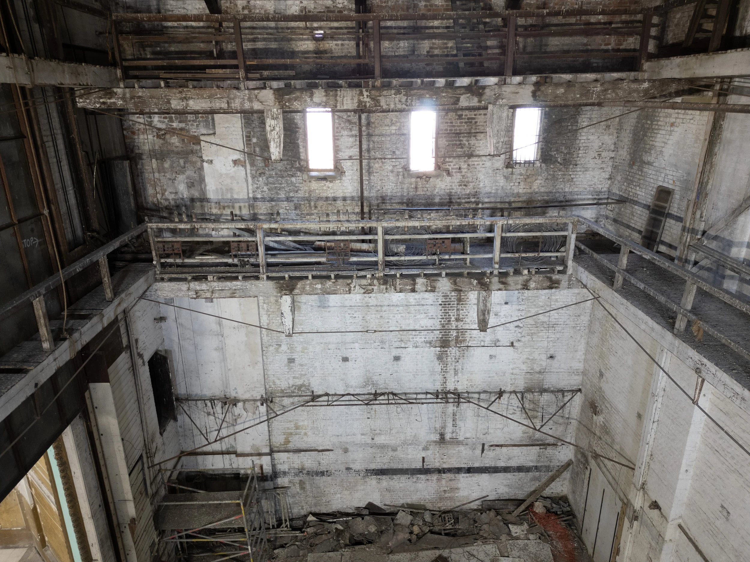 Interior of a dilapidated building with exposed brick walls, broken windows, and scaffolding. The space appears abandoned and in disrepair.