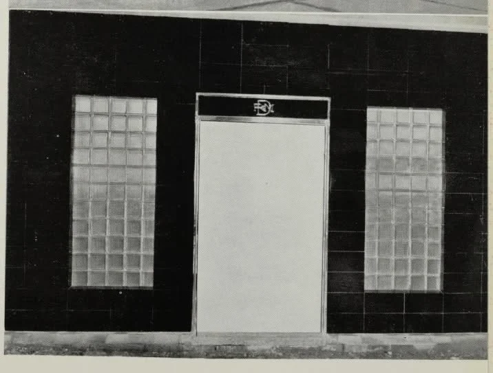 Black wall with two glass block windows flanking a door with an exit sign above.