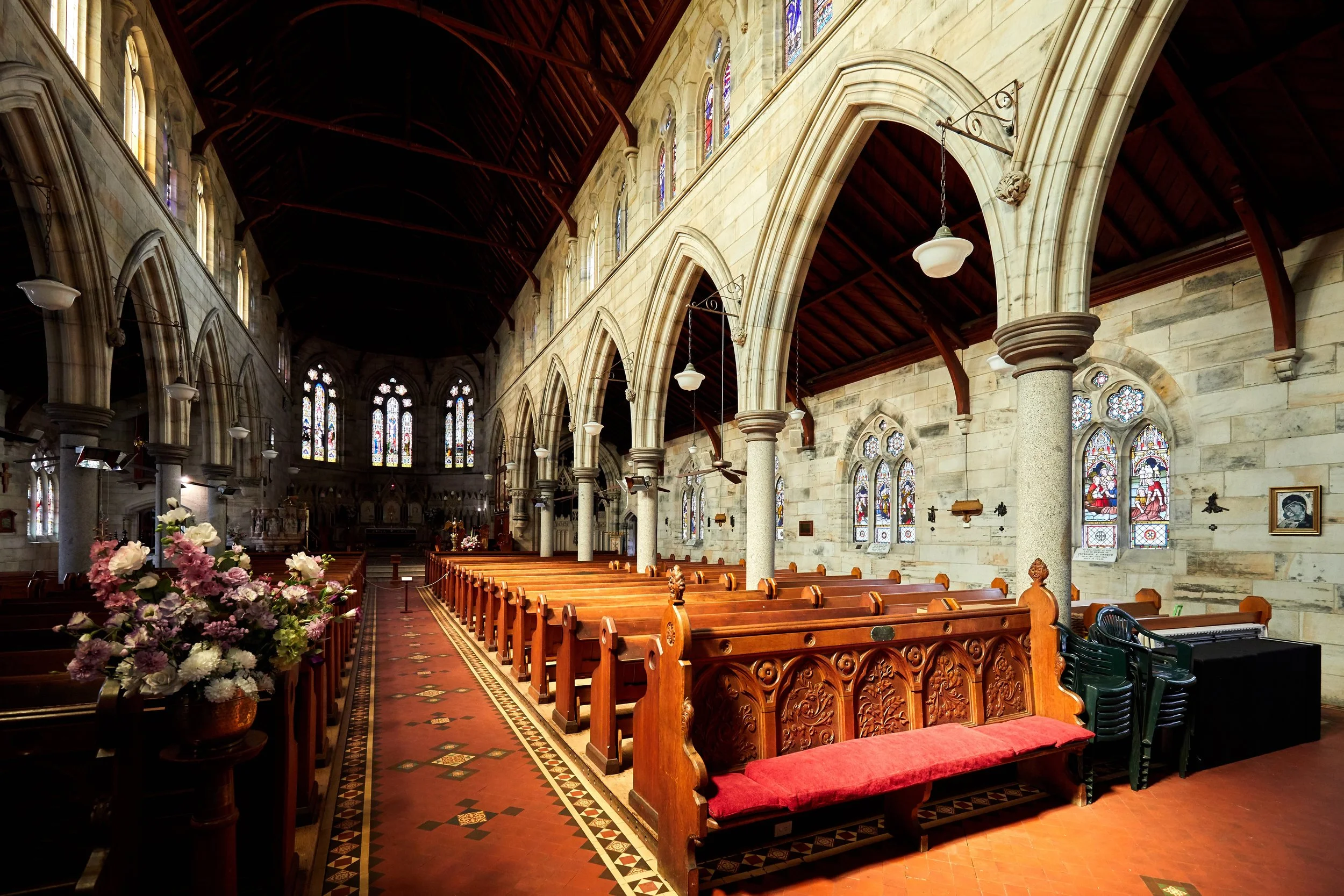 Interior of a church with wooden pews, stained glass windows, and a decorated flower arrangement in the foreground.