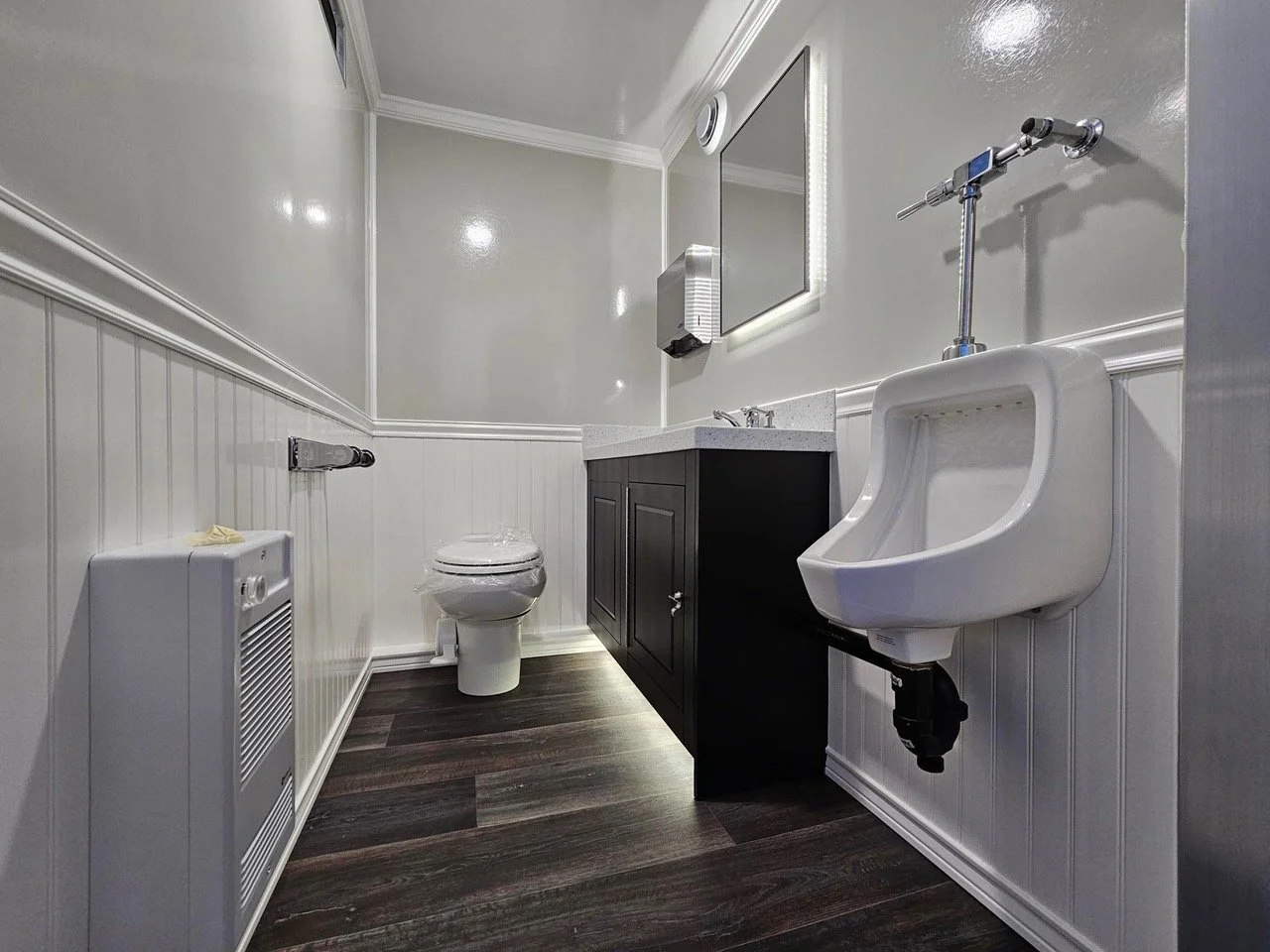 Restroom with a white toilet, a black vanity with a white countertop, a mirror, a urinal, and wooden floor.