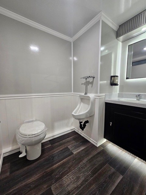 Bathroom with a toilet, urinal, black vanity with a mirror, and dark wood flooring.