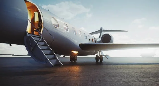 Private jet on runway with stairs leading into the cabin, under a partly cloudy sky.