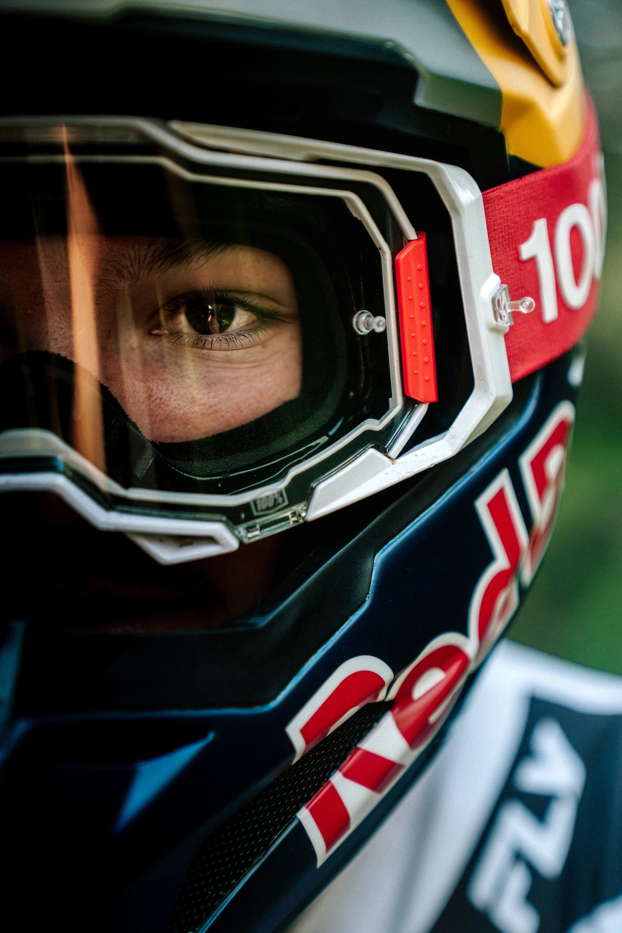 Close-up of a motocross helmet with a rider's eye visible through the goggles, featuring vibrant colors and a racing logo.