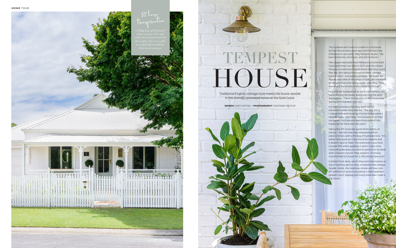 A white Victorian-style house with a white picket fence, green lawn, and a tree in front. The house has decorative trim around the porch.