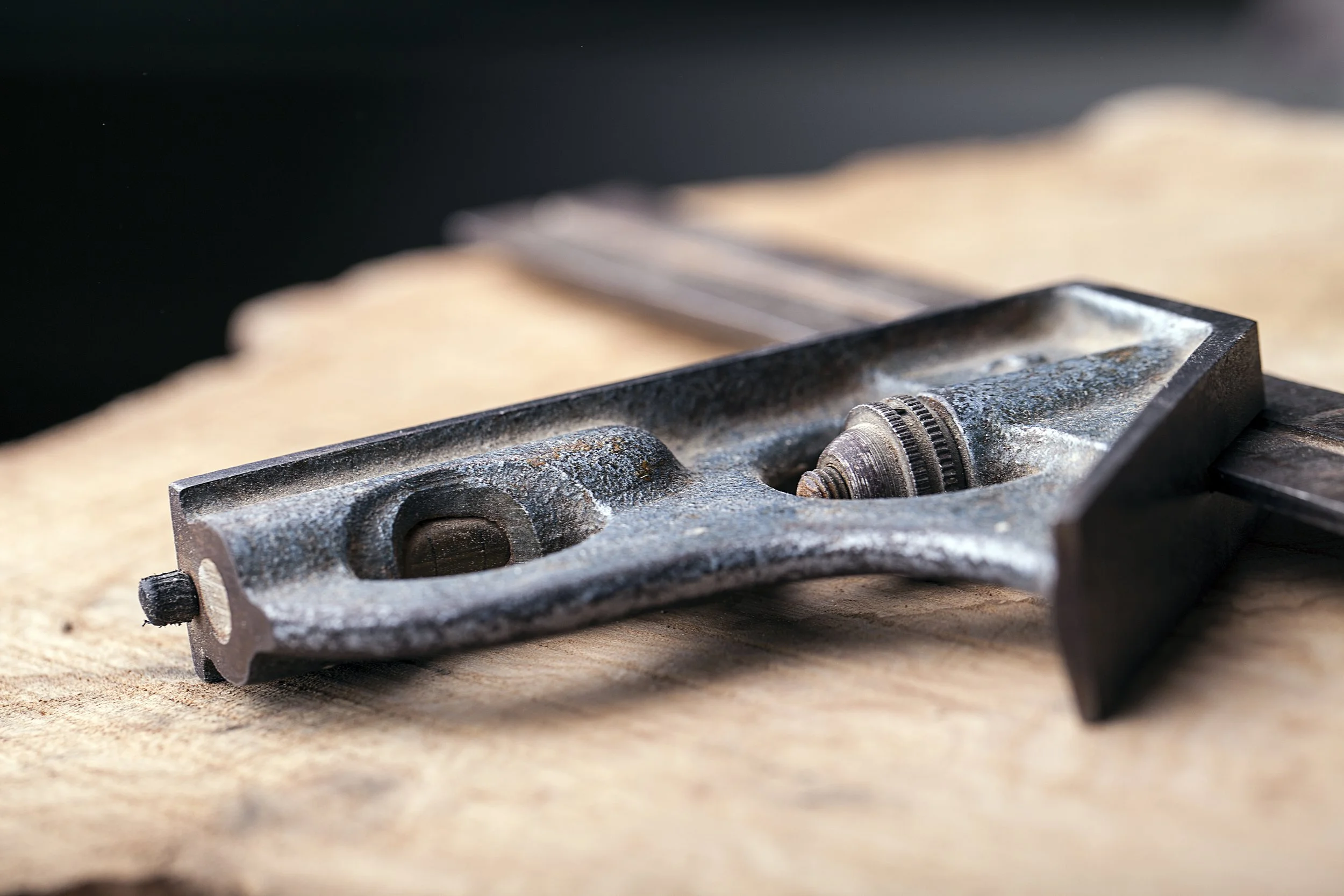 Close-up of a metal woodworking hand plane tool placed on a wooden surface, showing its blade and body.